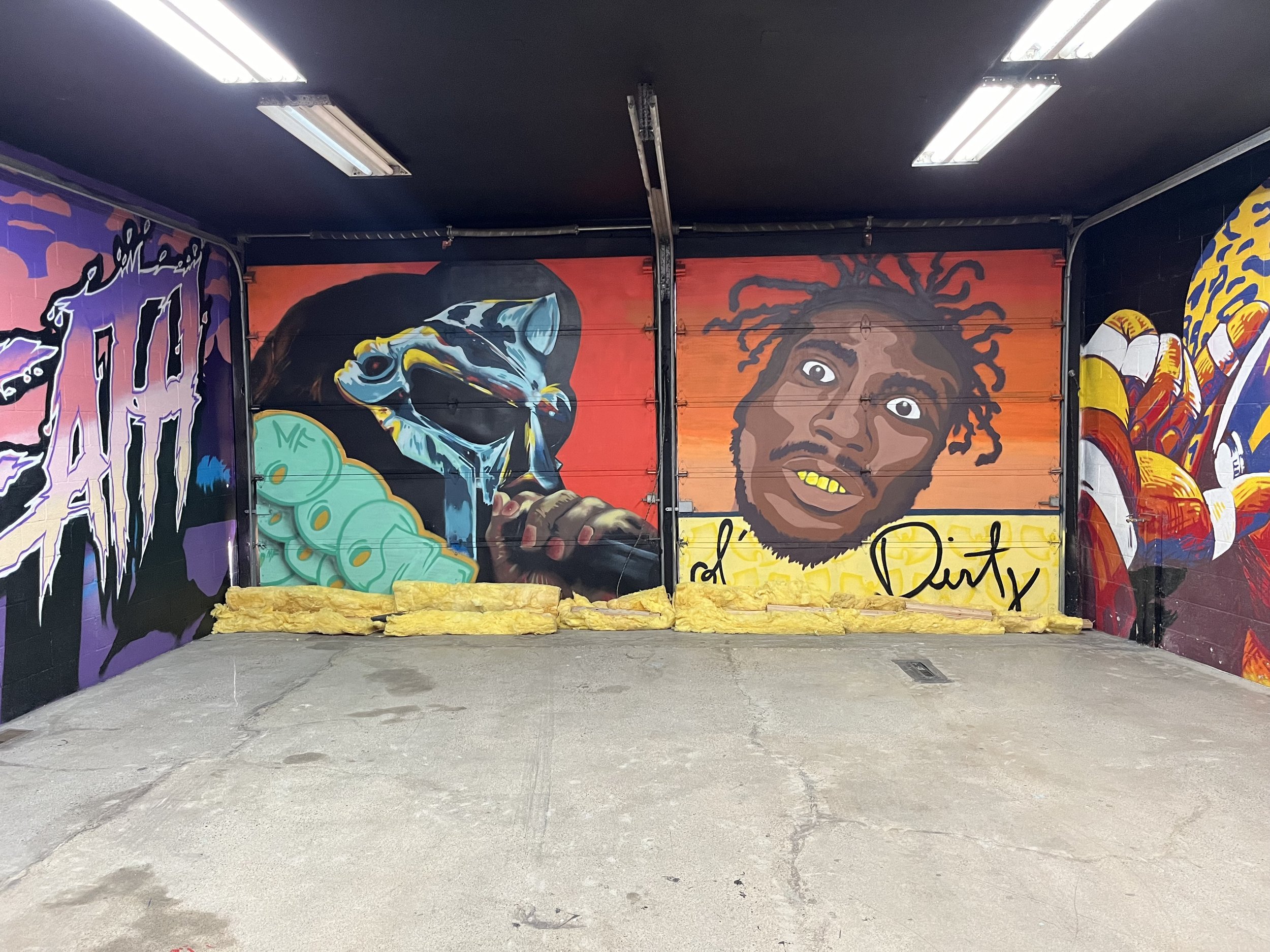 Magnificent graffiti art featuring political commentary and portraits of notable figures on garage doors inside a parking garage, with a textured concrete floor in the foreground.