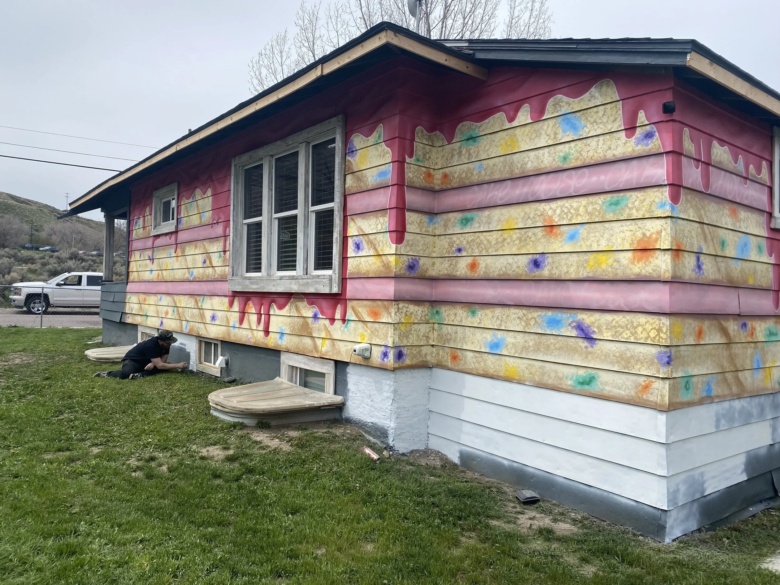 The house exterior is painted with colorful graffiti art, resembling a birthday cake rainbow sprinkles on pink and yellow background.