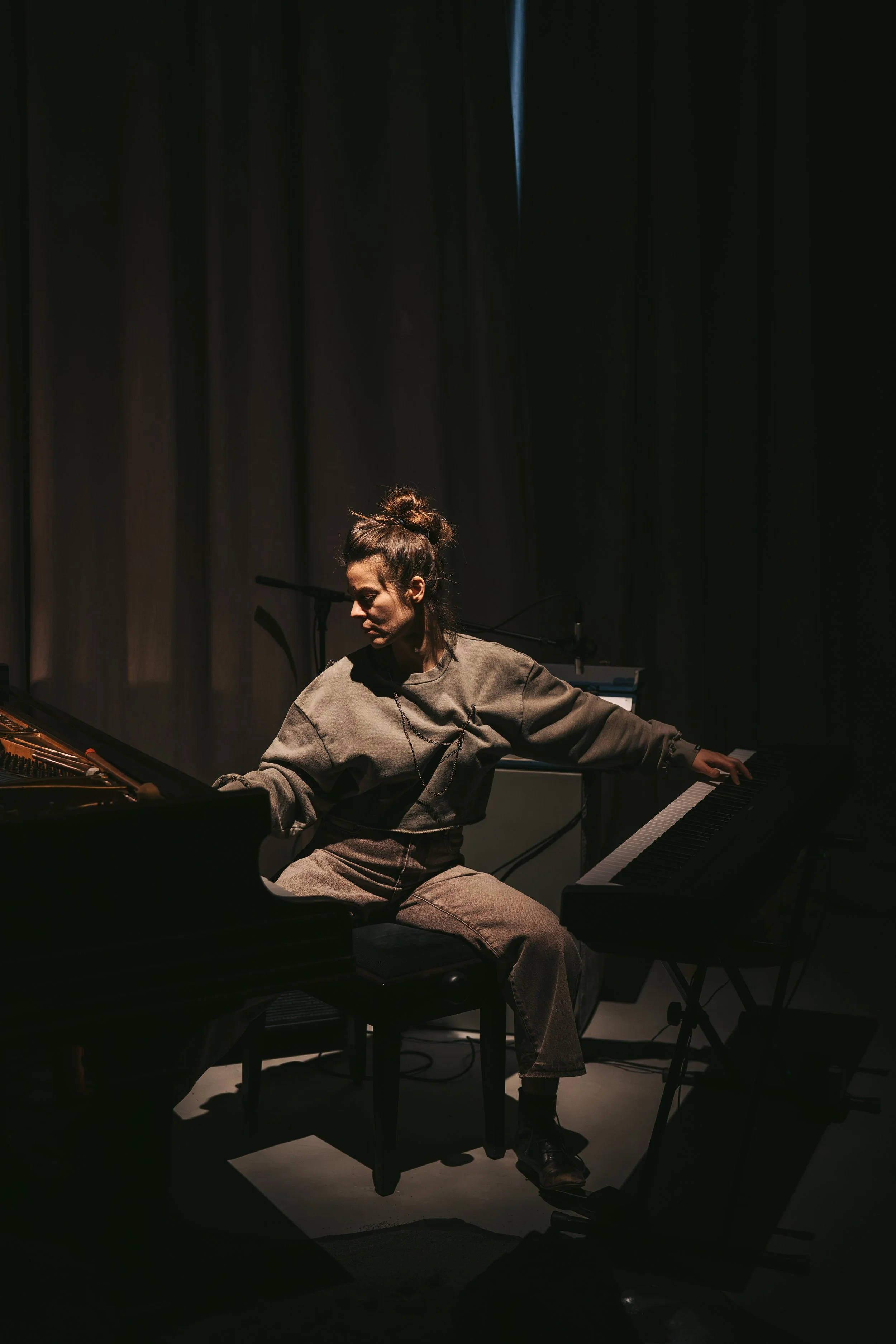 A woman sitting at a piano in a dark room, with a spotlight on her and the piano.