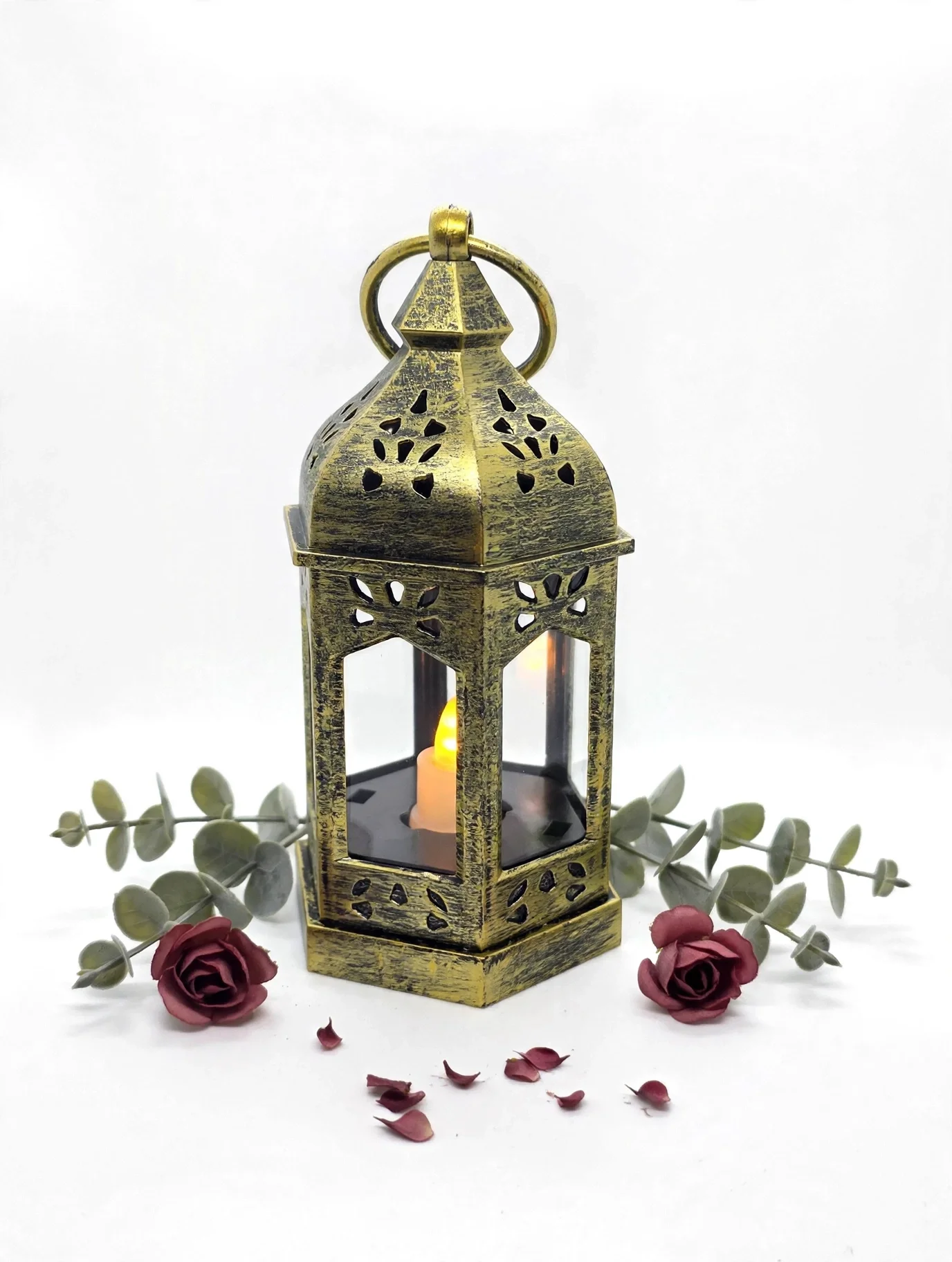 Vintage gold lantern with glowing candle, roses, eucalyptus, and scattered petals