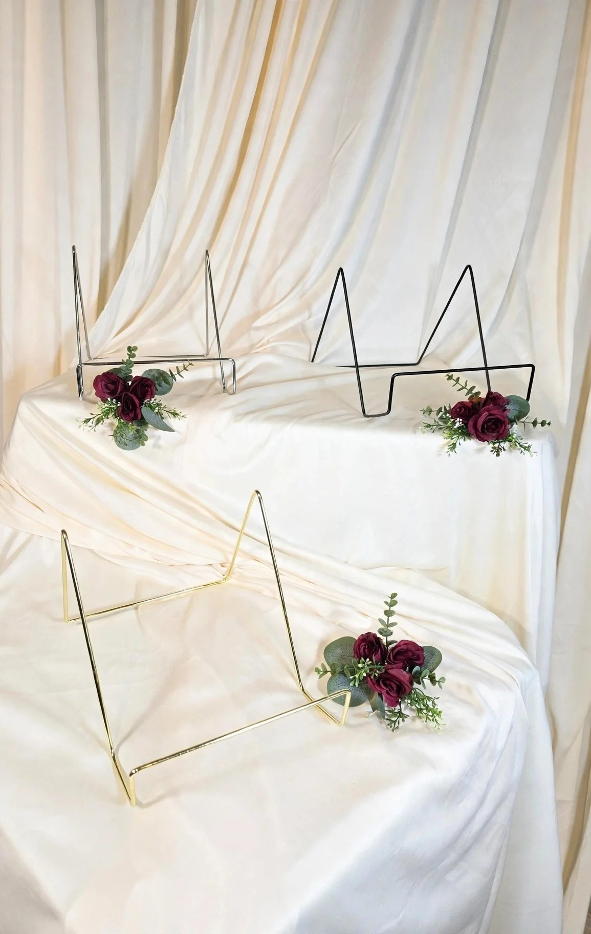 Gold, silver, and black metal easel stands with burgundy roses and greenery