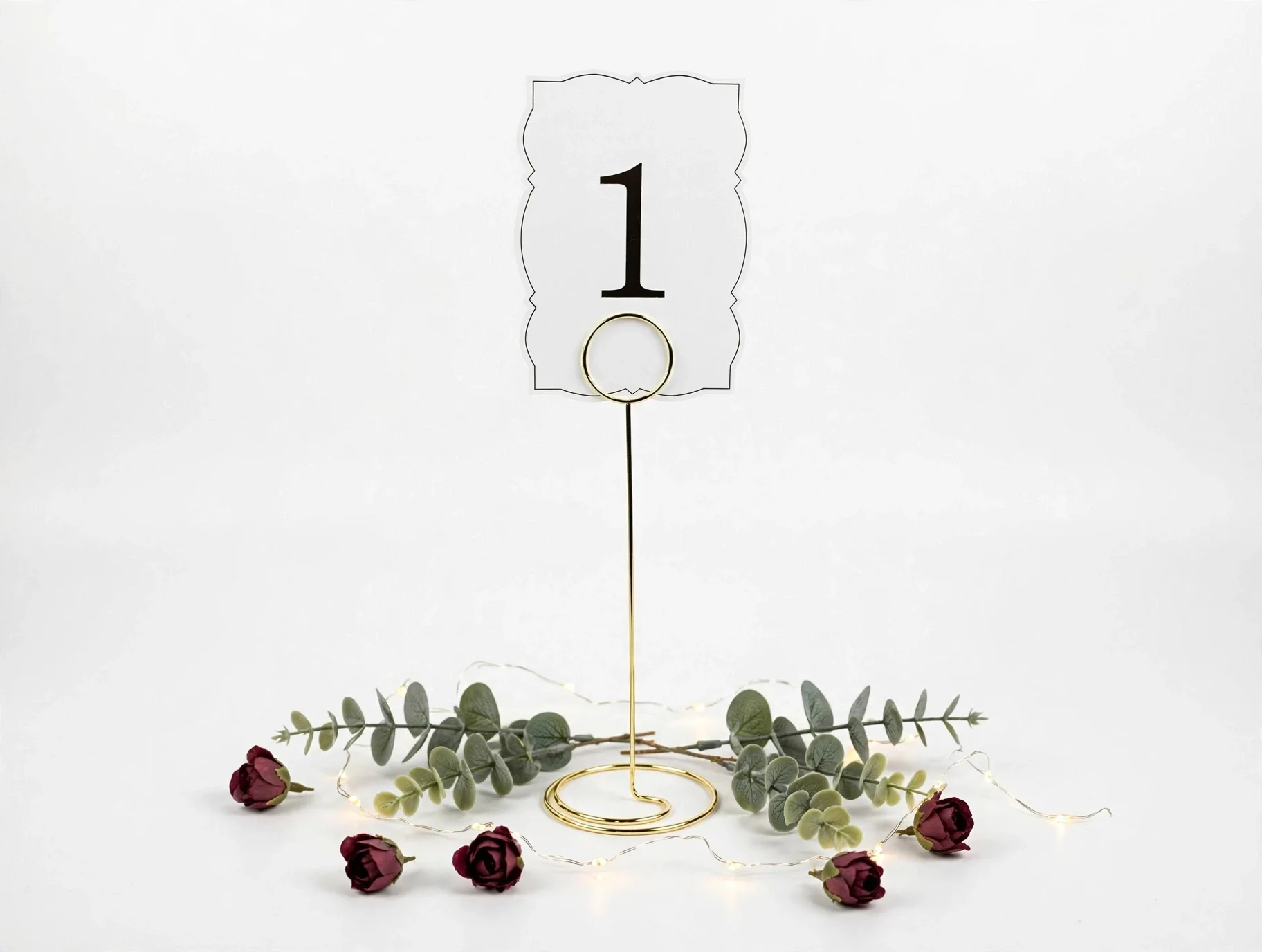Metal gold table number stand with card number one, roses, eucalyptus, and fairy lights