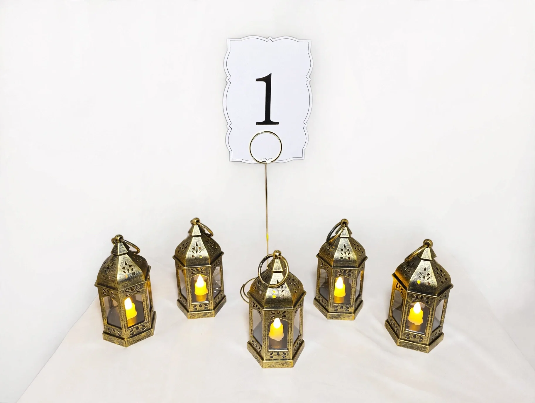 5 vintage gold lanterns with glowing candle, roses, eucalyptus, and scattered petals, with table number