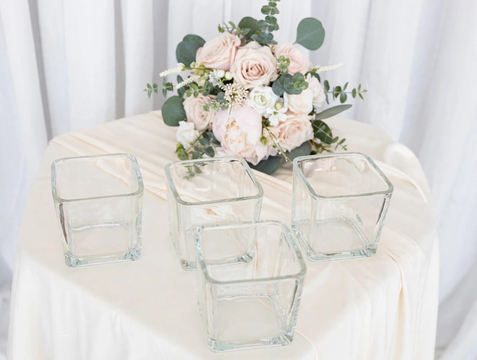 Four clear square glass vases with pink rose bouquet and greenery backdrop