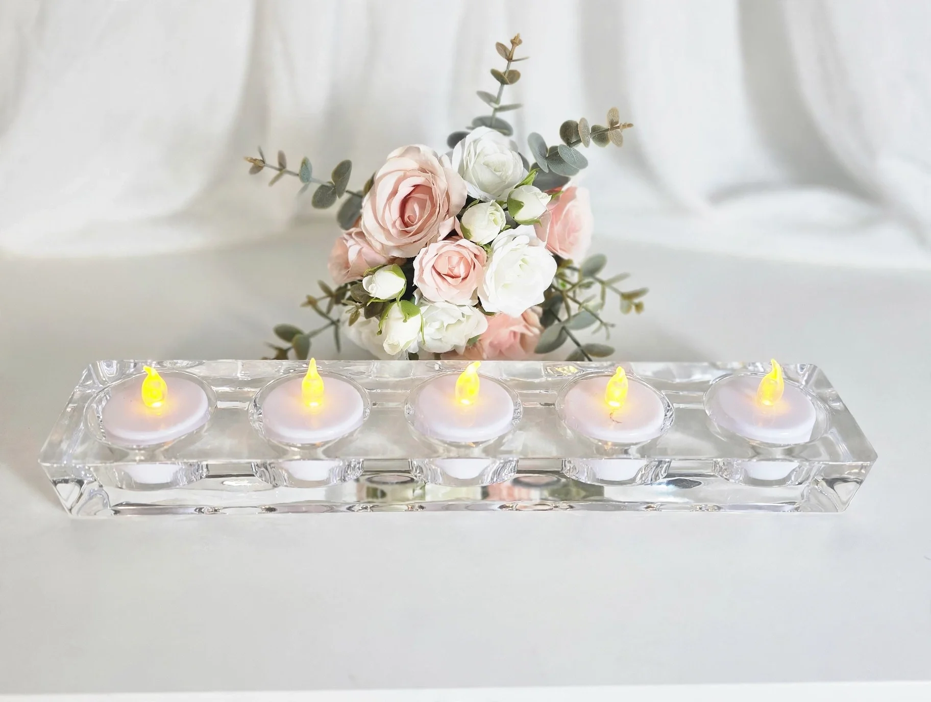 Rectangular glass candle holder with five glowing candles and pink rose bouquet