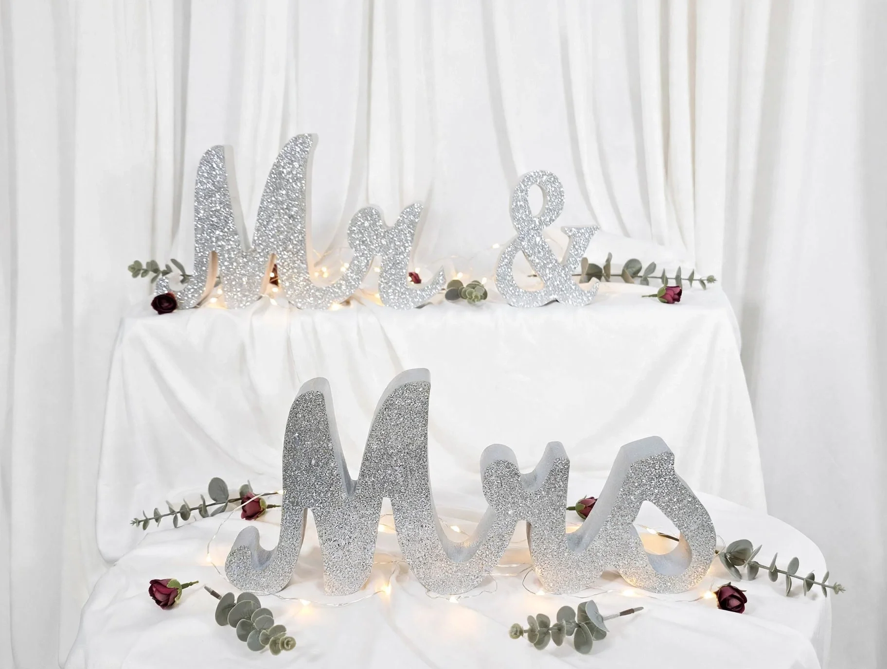 Silver glitter Mr and Mrs letters with roses and lights on white draped fabric