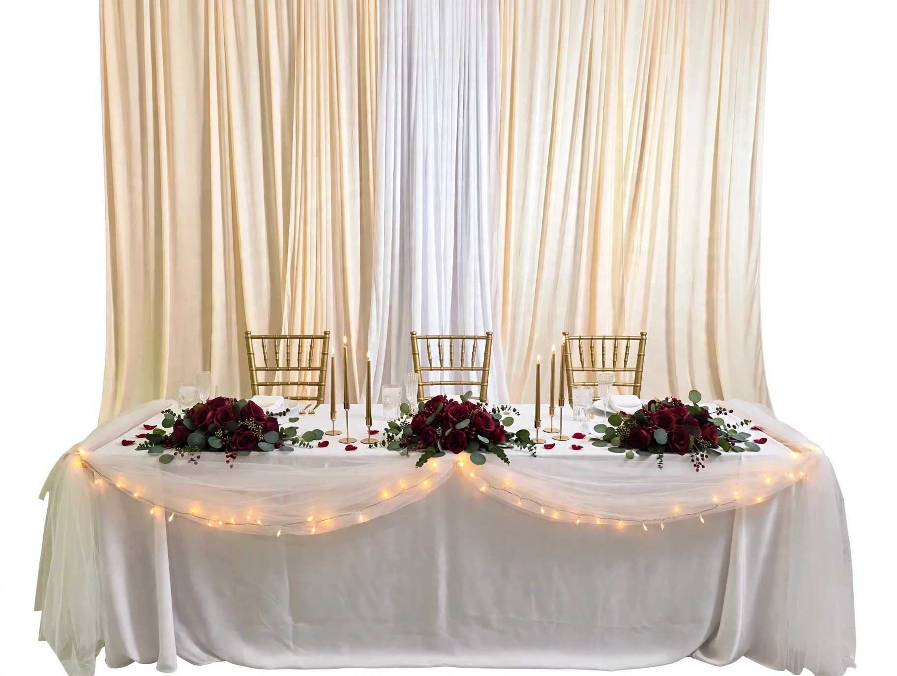 Elegant wedding table with gold chairs, red floral centerpieces, candles, and draped backdrop