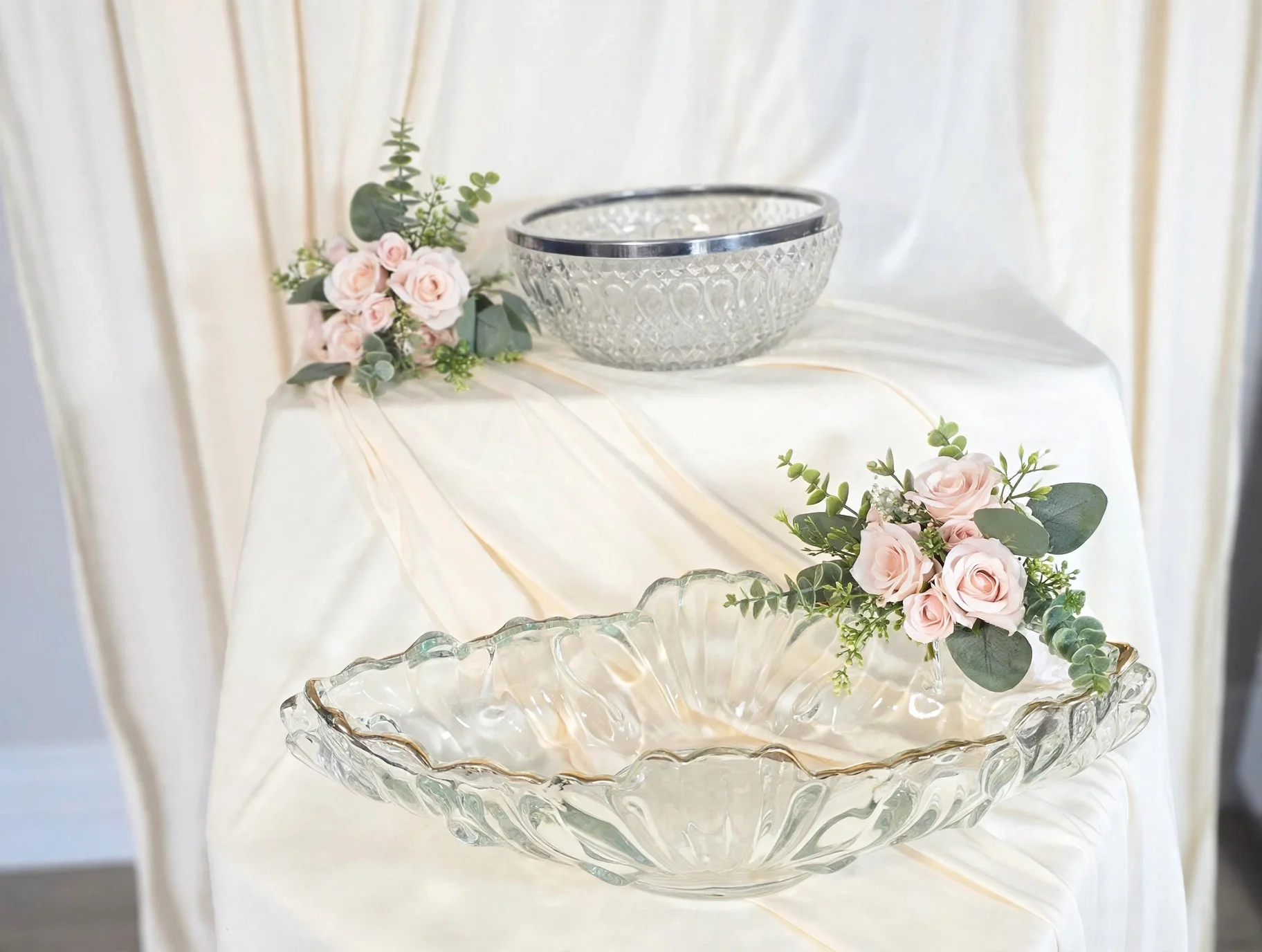 Clear glass bowls with pink roses and greenery on cream draped fabric
