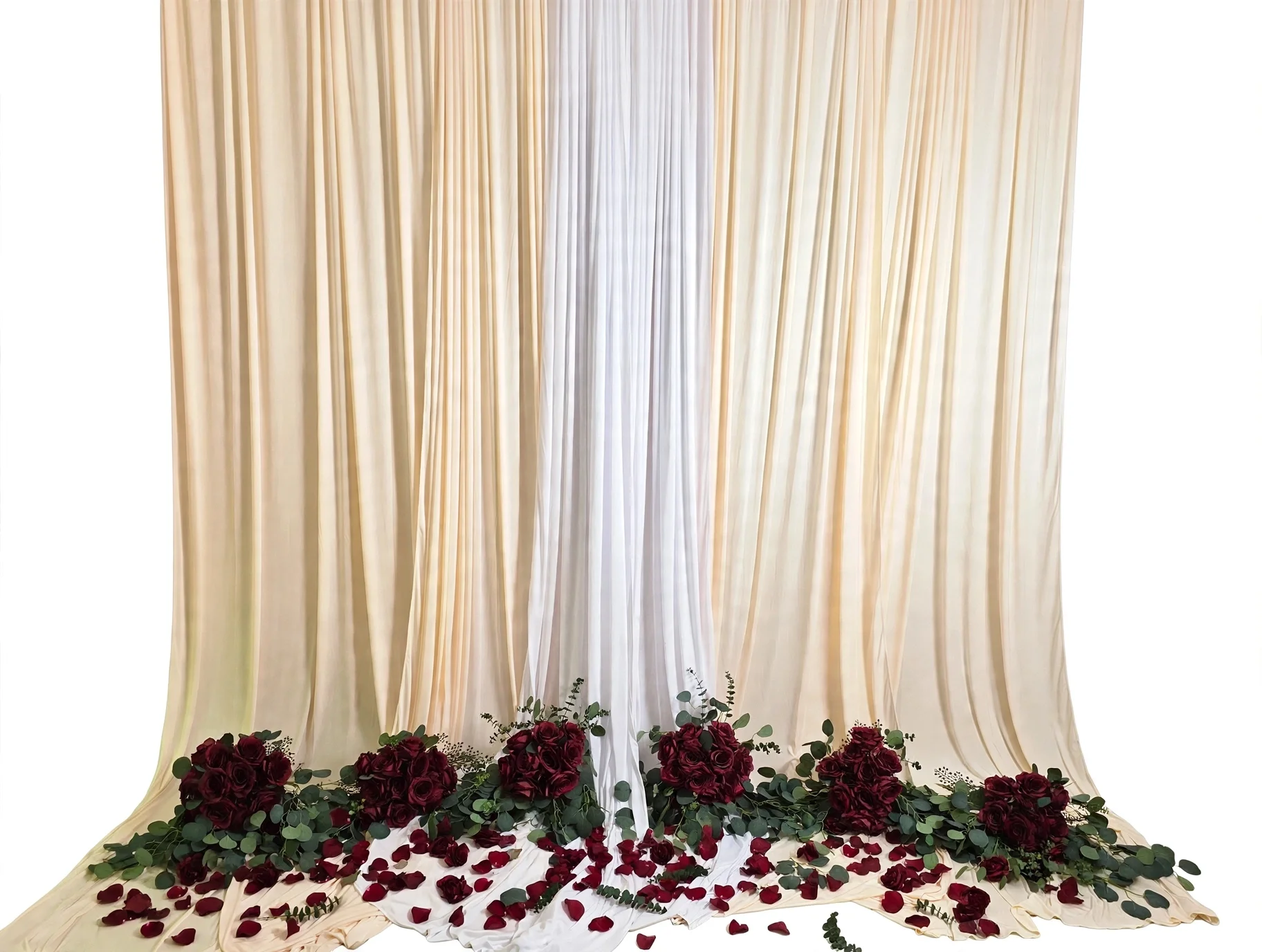 Cream and white draped backdrop with red roses, eucalyptus, and scattered petals