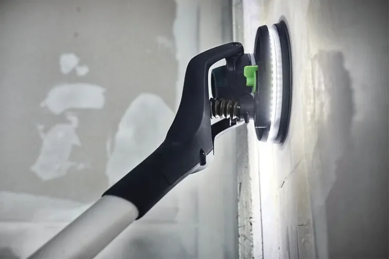 A person using a drywall sander with a circular sanding disc to smooth a wall.