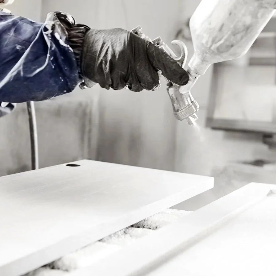 A person wearing a black glove using a spray gun to apply a coating or paint on a white surface.
