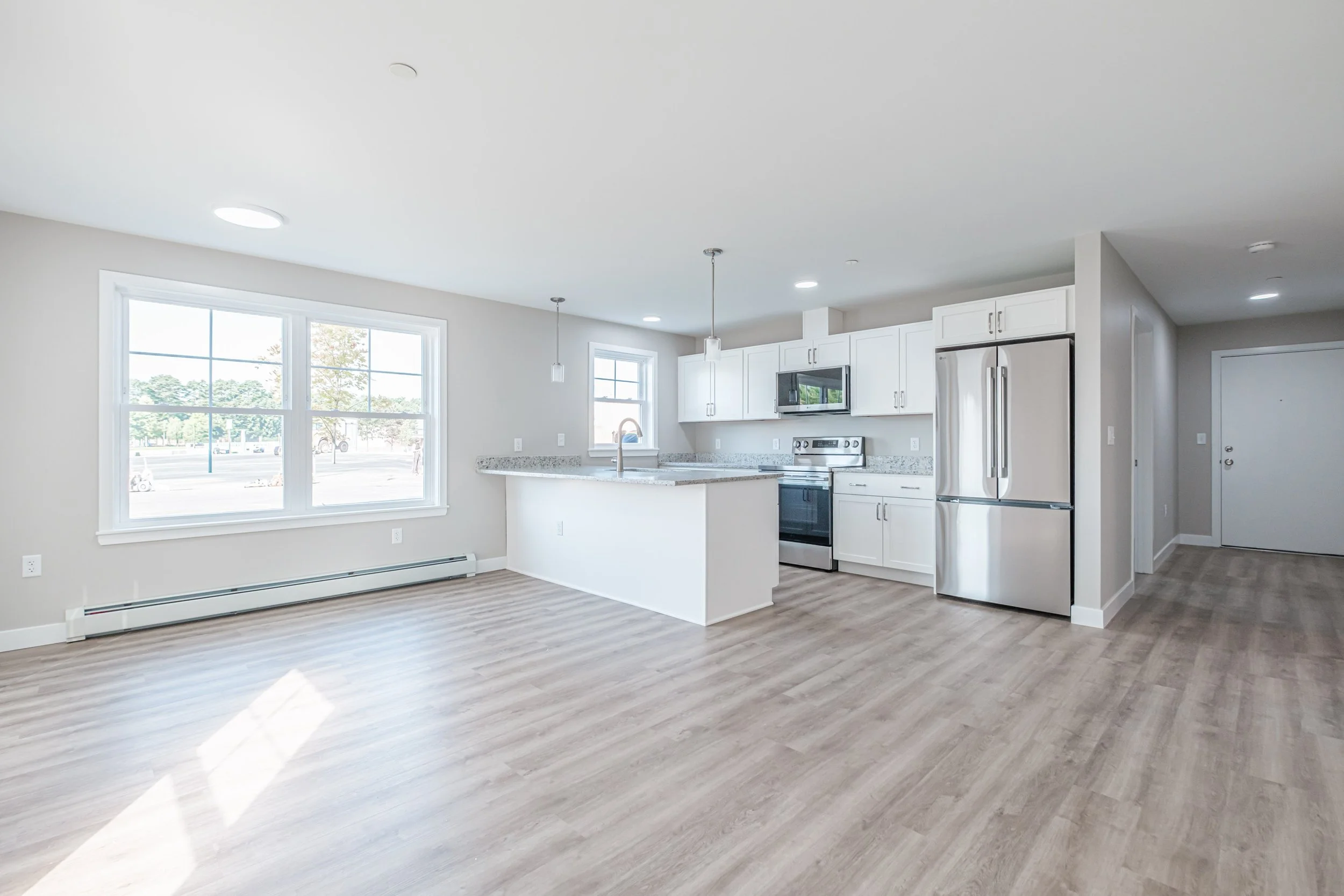 New-construction condo with an open-concept kitchen and living area, contemporary finishes, stainless steel appliances, and large windows.