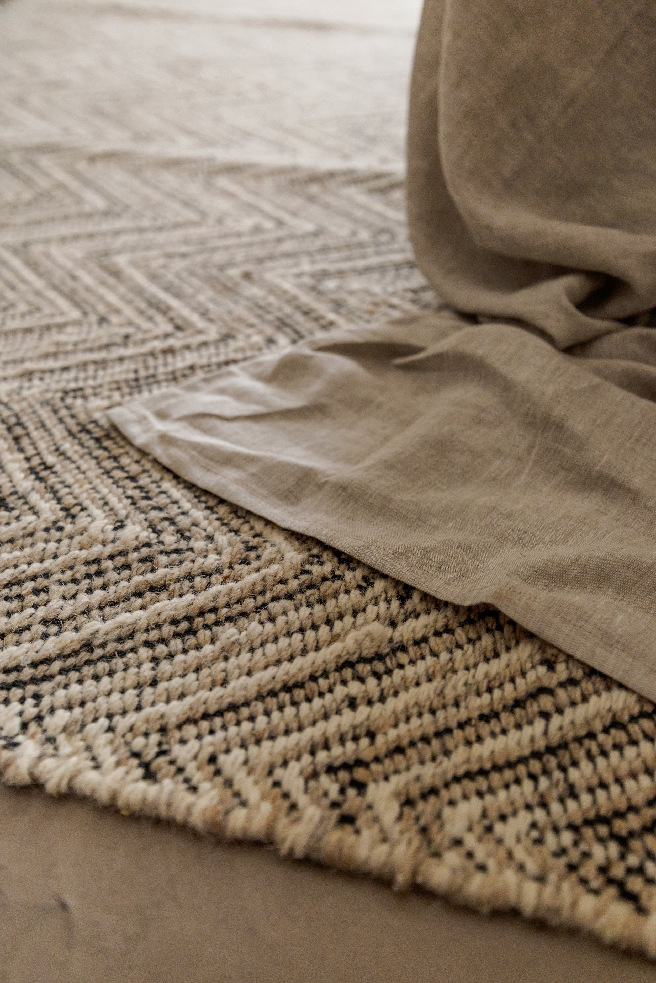 Close-up of a textured beige and black woven rug with folded beige fabric on top.