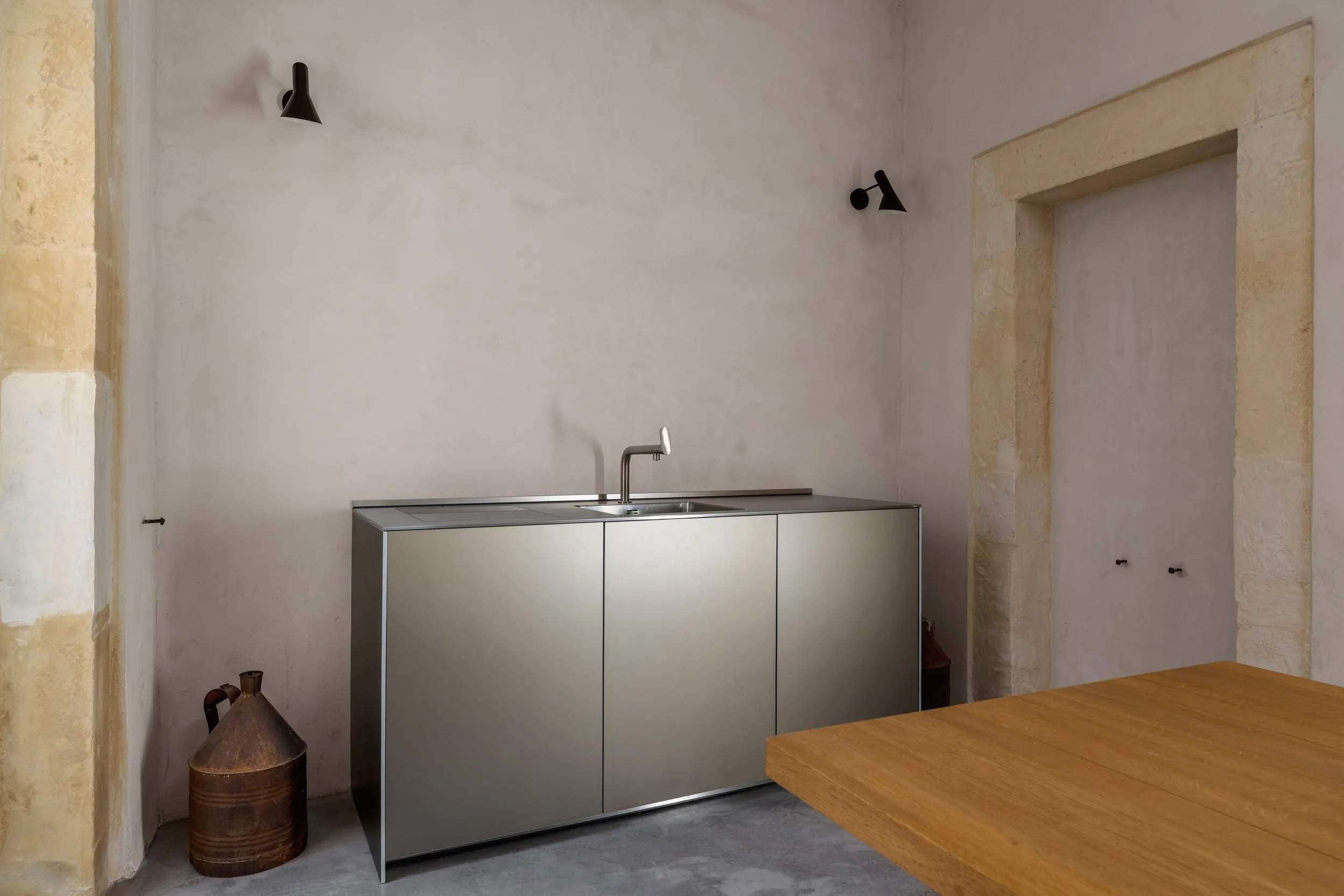 Minimalist kitchen corner with stainless steel cabinet, sink, and modern black wall-mounted lights.