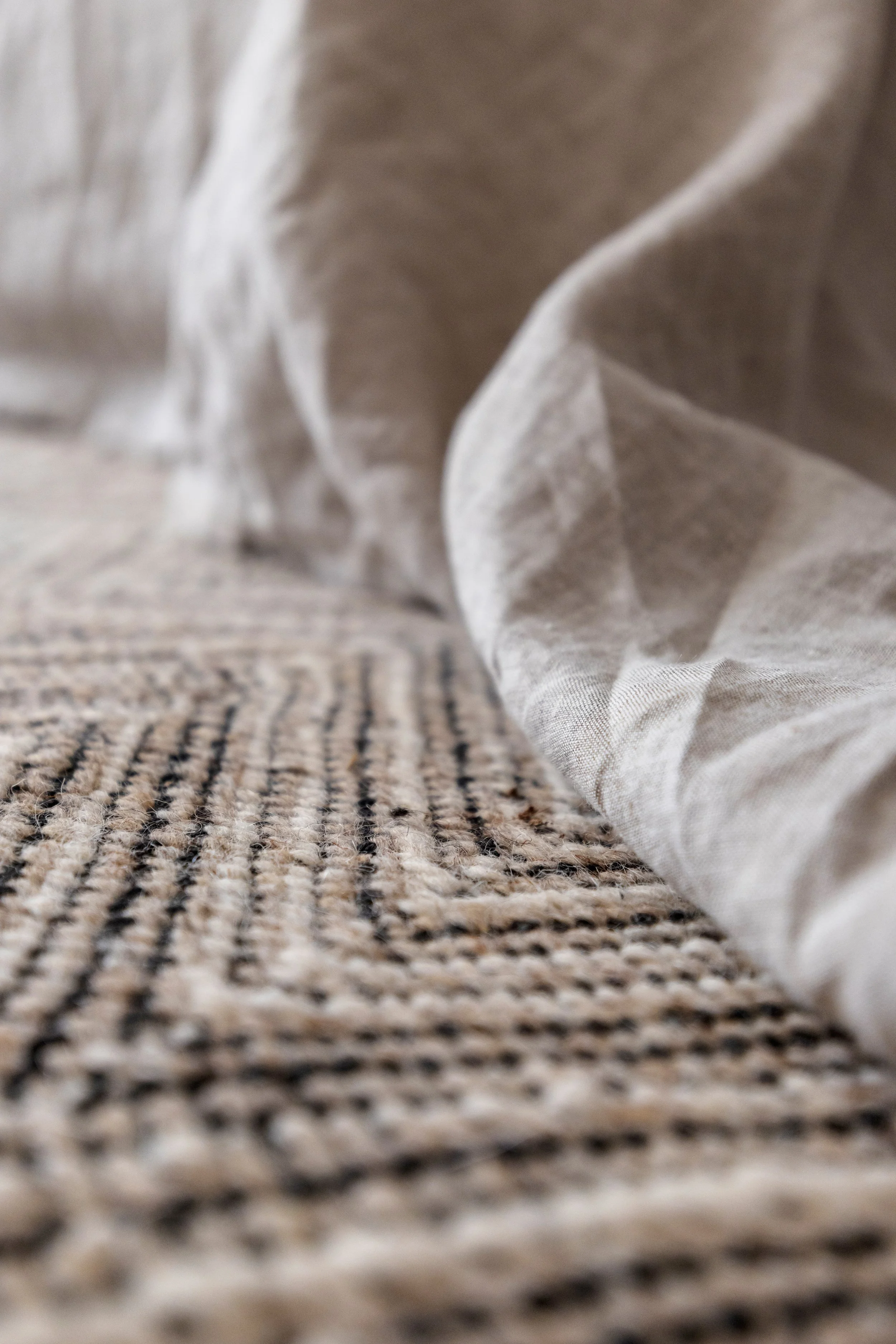 Close-up of a textured woven carpet with a piece of crumpled light-colored fabric resting on it.