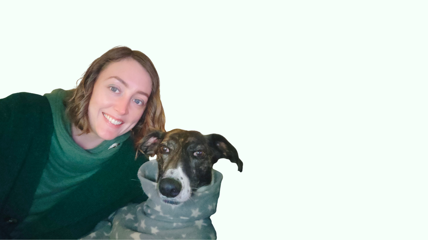 A woman with shoulder-length wavy hair smiling next to a black and white dog wearing a gray hoodie with white stars, against a light green background.