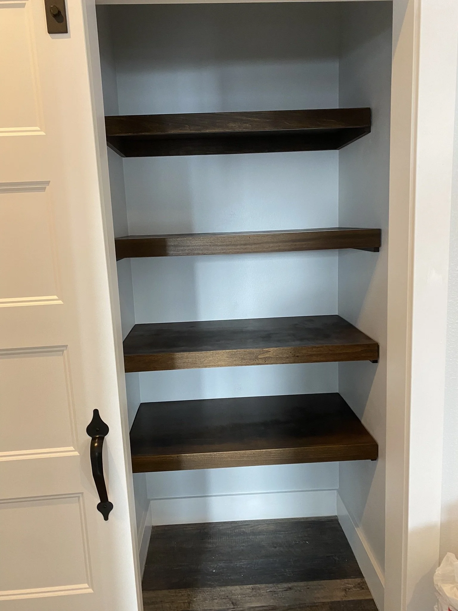 Empty closet with four dark wood shelves and white walls, part of a room with a white door on the left.