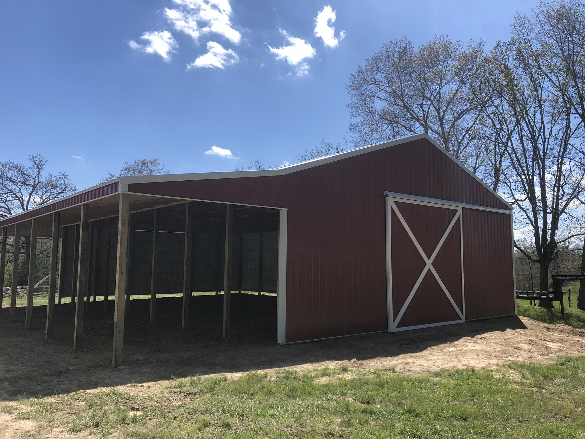 A red barn-style building with white trim and a large sliding door, under a blue sky with a few white clouds and surrounded by leafless trees.