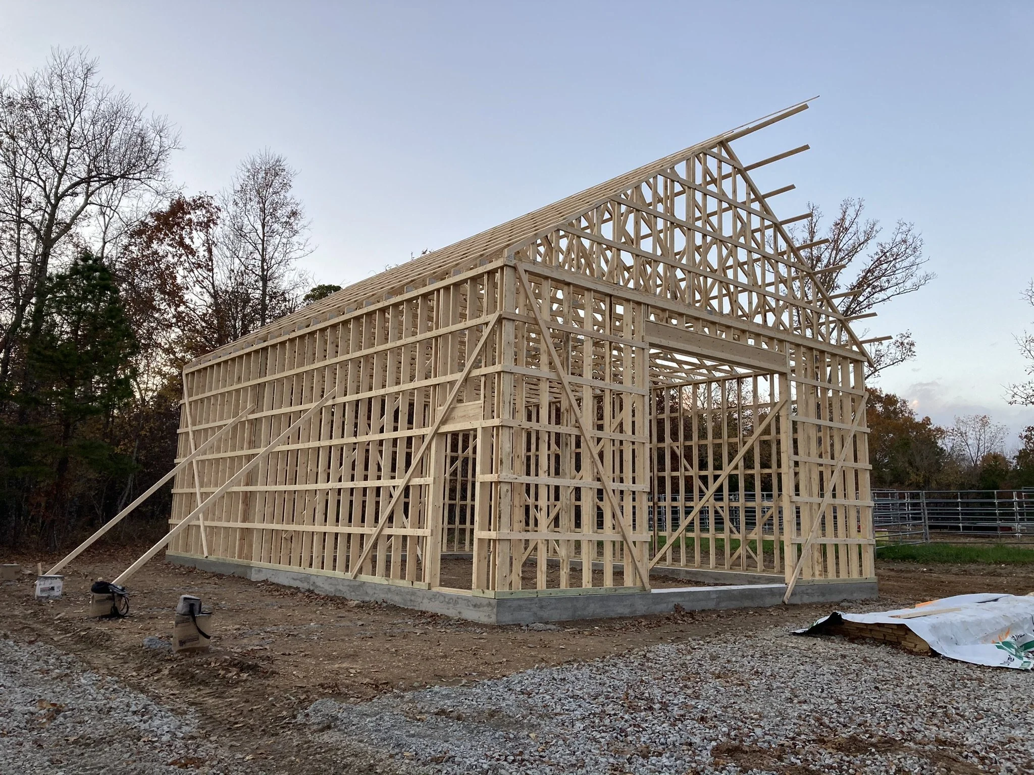 Wooden house frame under construction with surrounding trees and a clear sky.