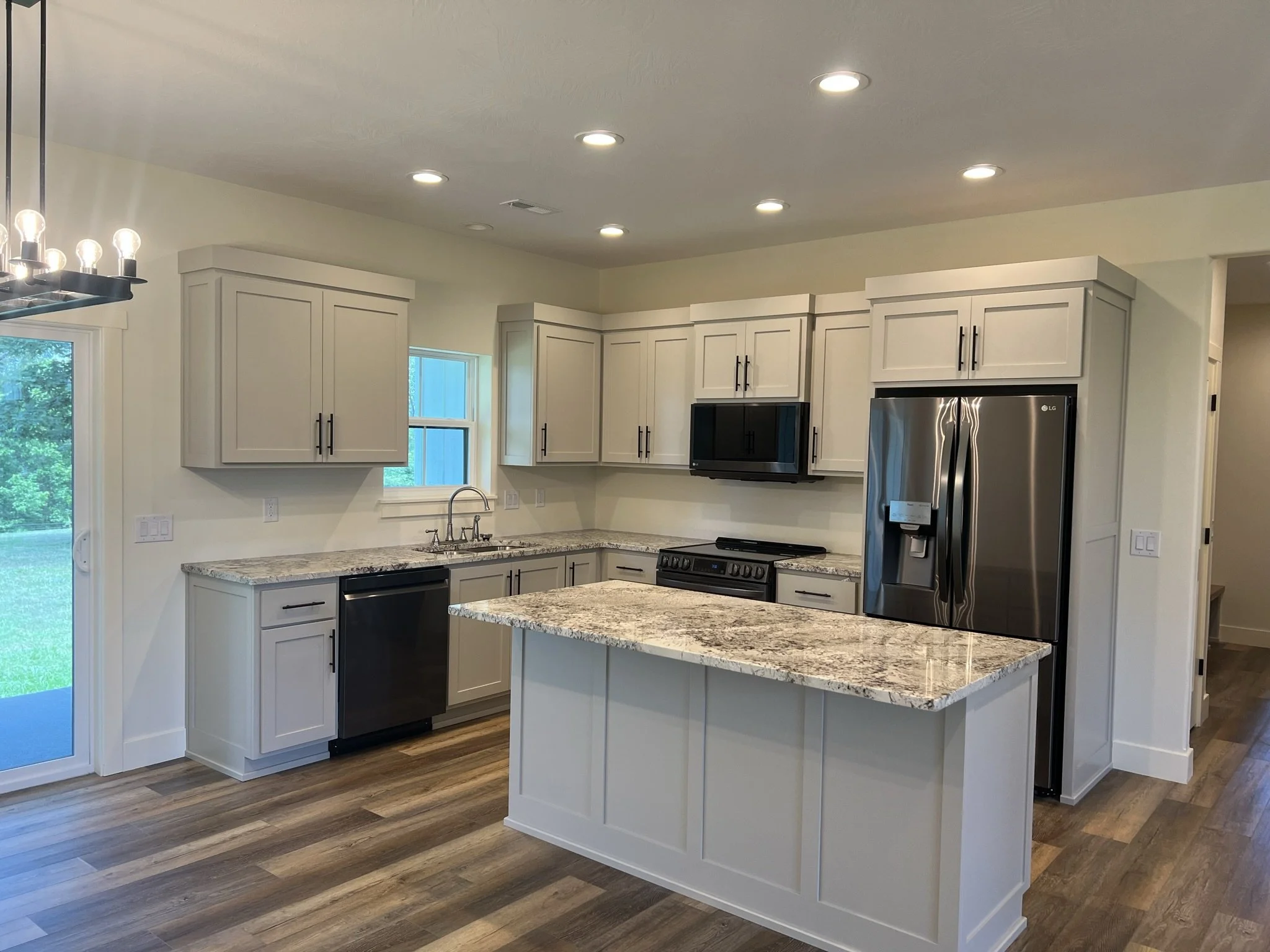 Modern kitchen with white cabinetry, granite countertops, stainless steel appliances, hardwood floors, large windows, and ceiling recessed lighting.