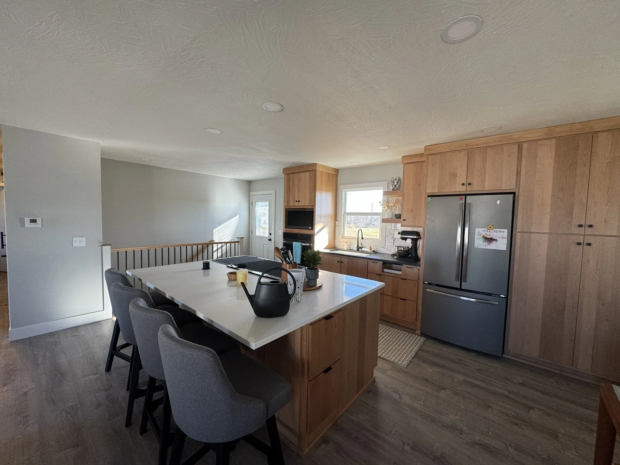 Open-concept kitchen and dining area with wooden cabinets, a stainless steel refrigerator, and a large white dining table surrounded by gray chairs.