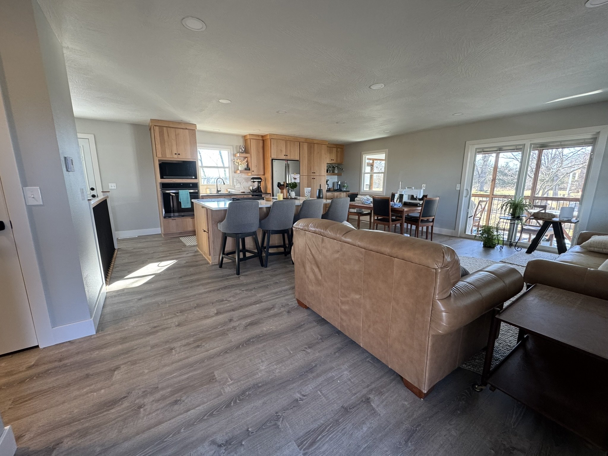 Open-concept living room and kitchen with hardwood floors and large windows showing outdoor scenery.