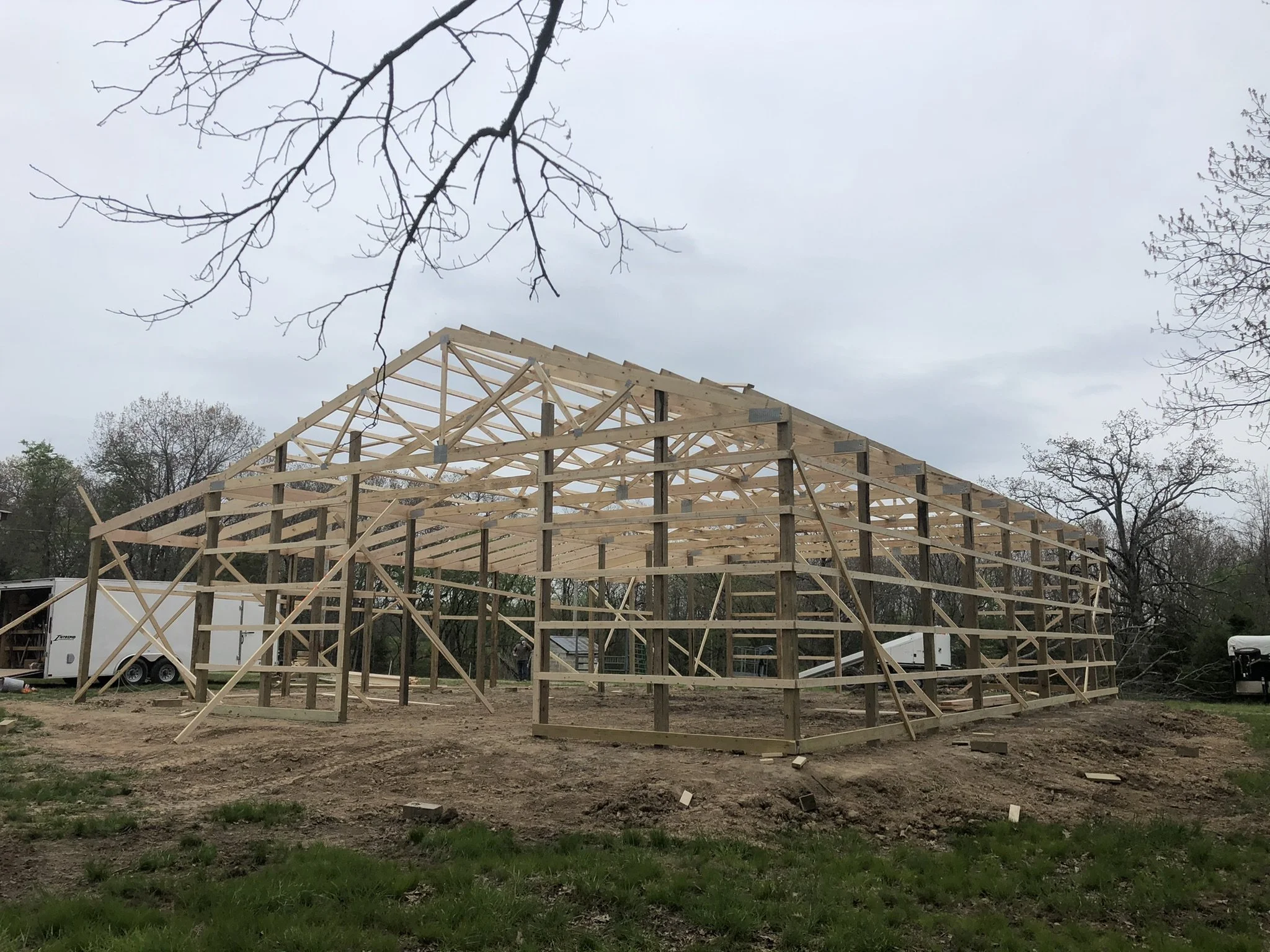 A house under construction with a wooden framework and a cloudy sky overhead, surrounded by trees and construction equipment.