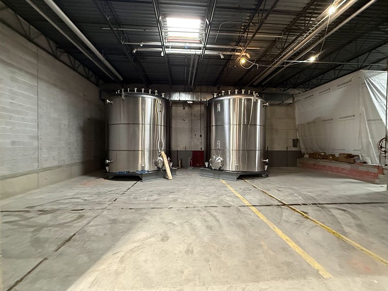 Two large stainless steel tanks inside a warehouse or industrial facility.