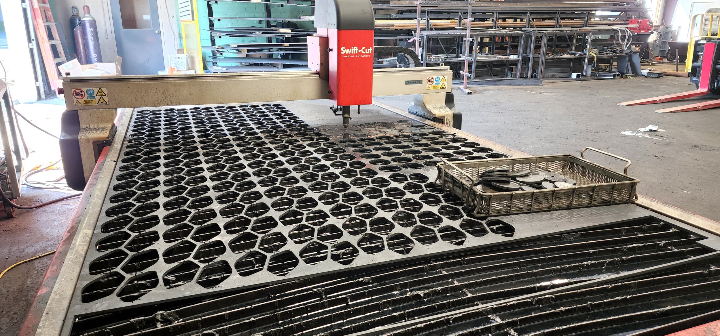 Laser cutting machine in a workshop with metal parts on a honeycomb cutting bed.