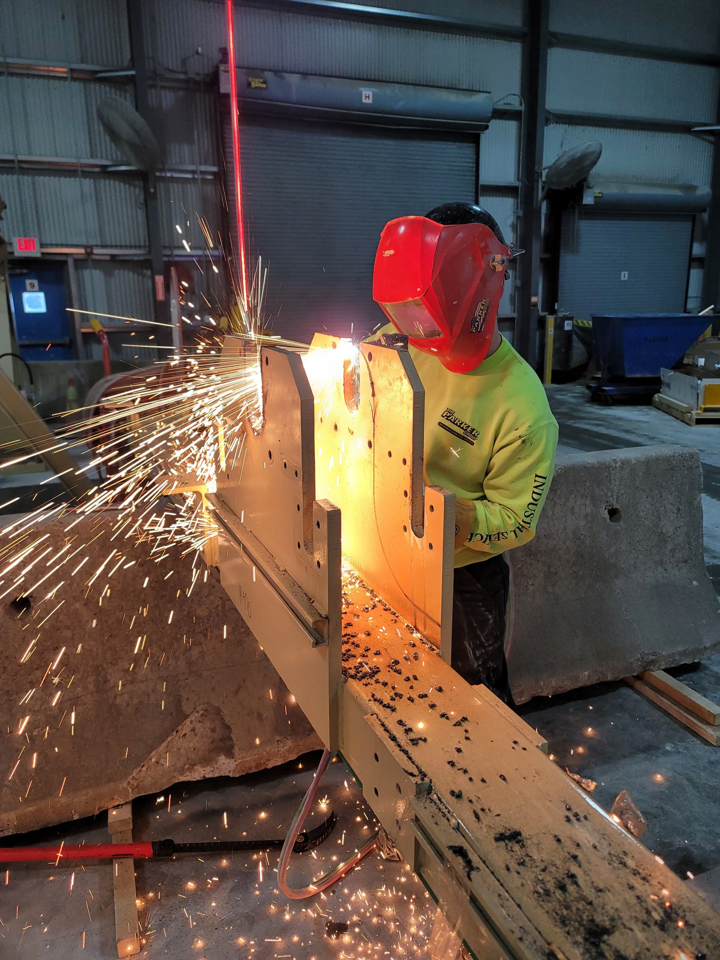 A person wearing safety gear welding metal in an industrial setting, sparks flying from the welding process.