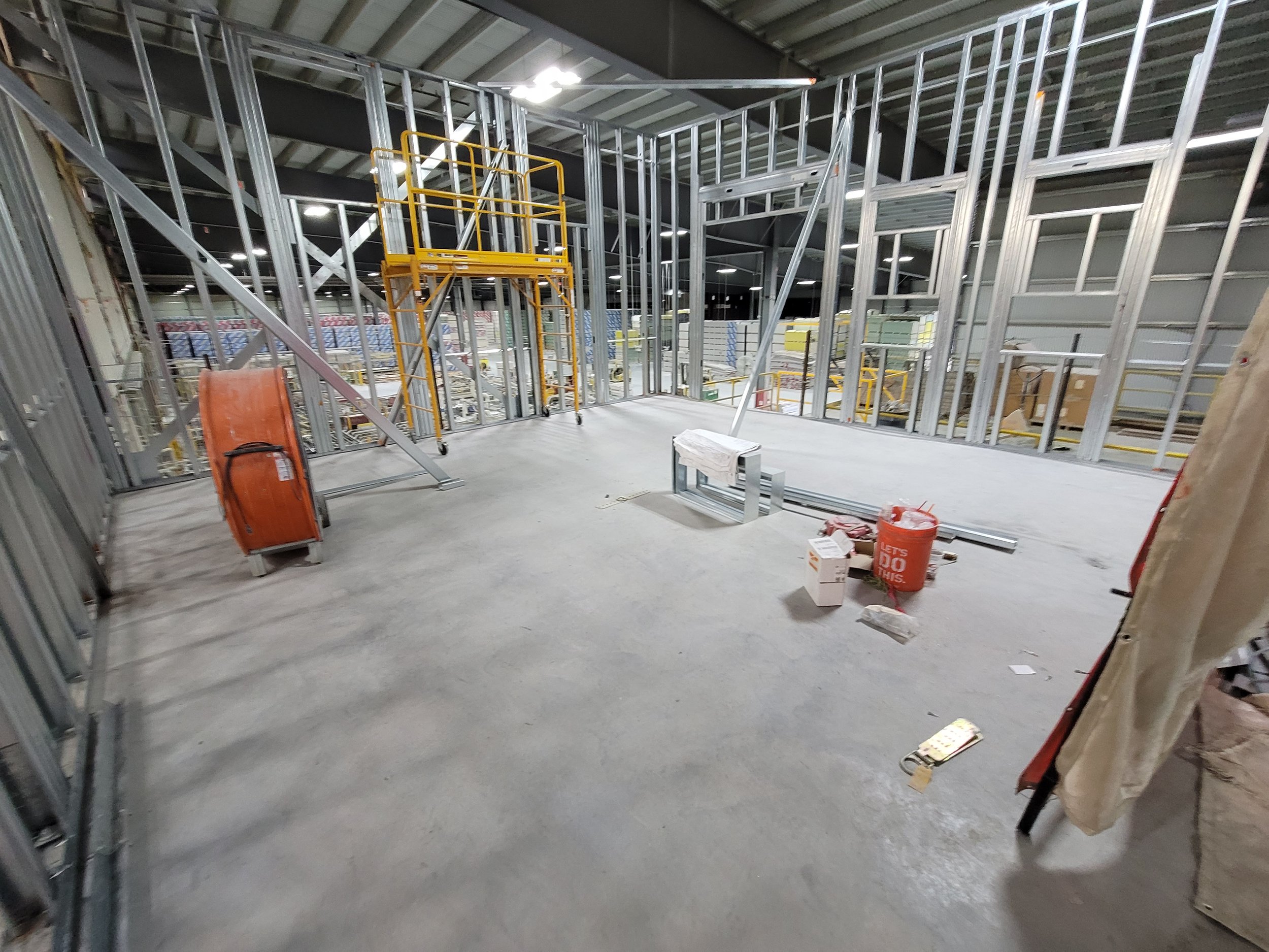 Construction inside a building with metal framing, a yellow ladder, and construction tools and supplies scattered on the floor.