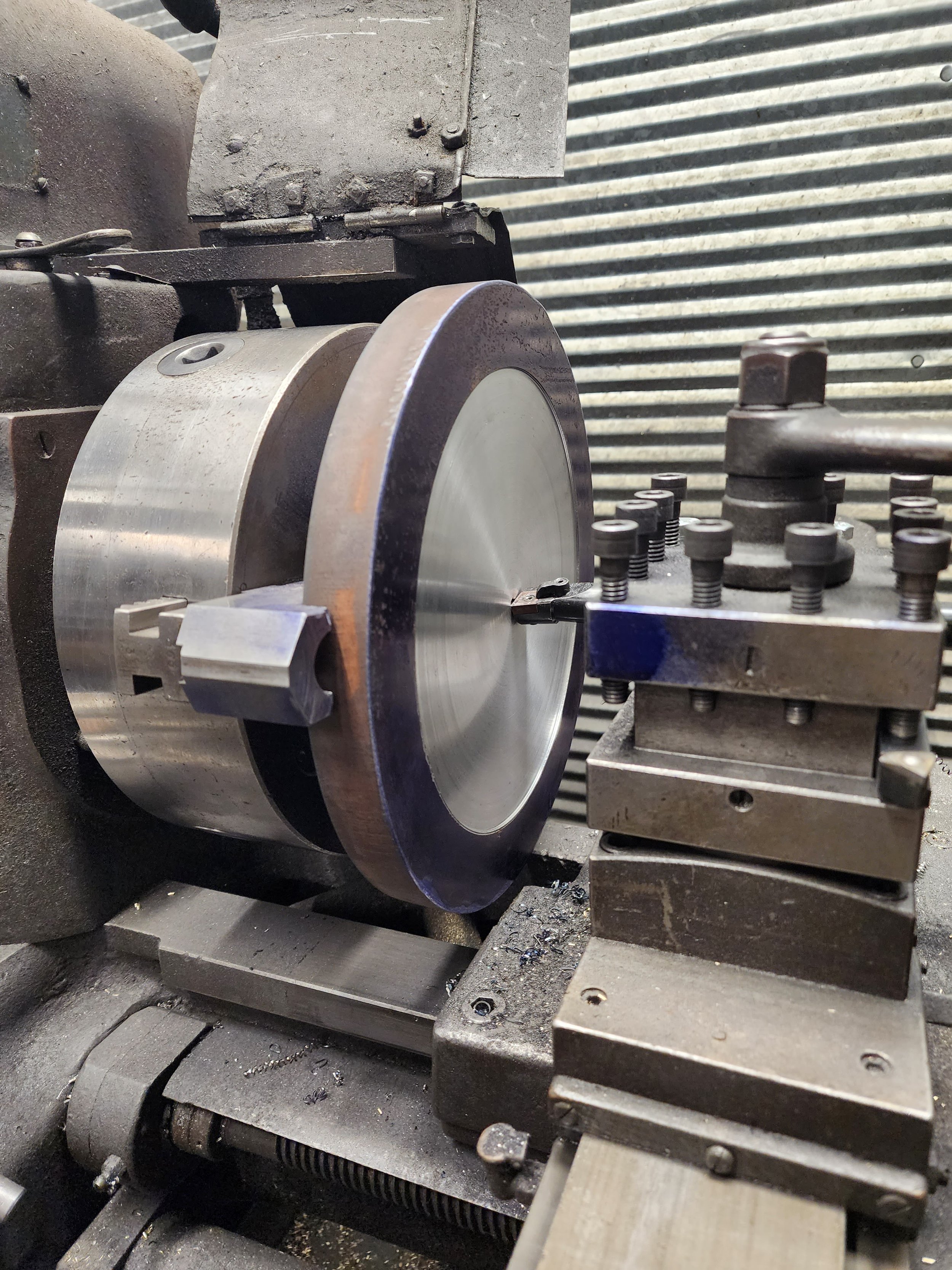 Close-up photo of industrial machinery, including a large metallic disk, screws, bolts, and various metal components in a workshop or factory setting.