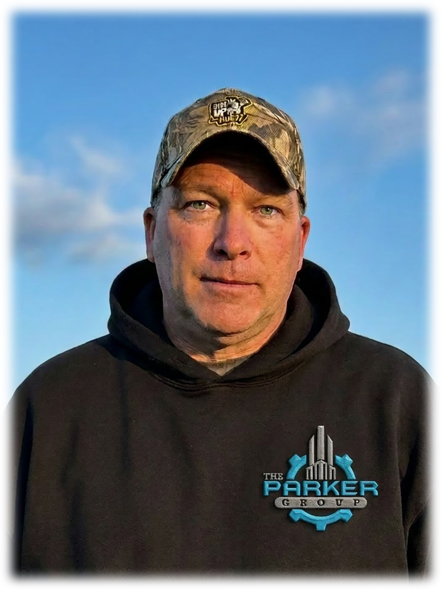 A man wearing a camouflage cap and a black hoodie with a logo that says "The Parker Group" stands outdoors against a blue sky with some clouds.