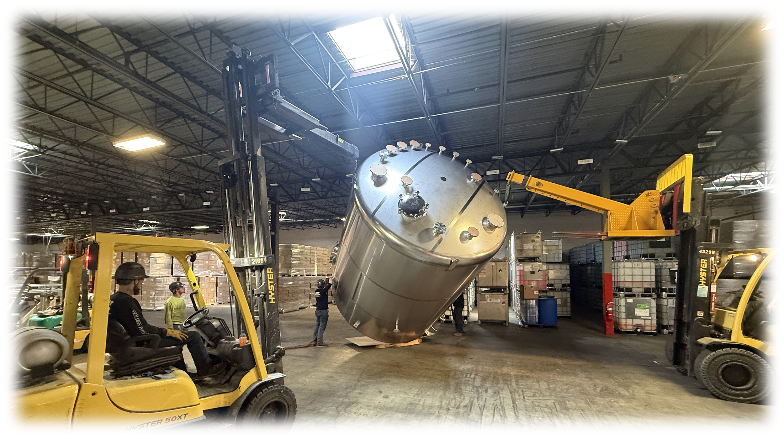 Workers and forklifts in a warehouse installing or inspecting a large industrial tank.