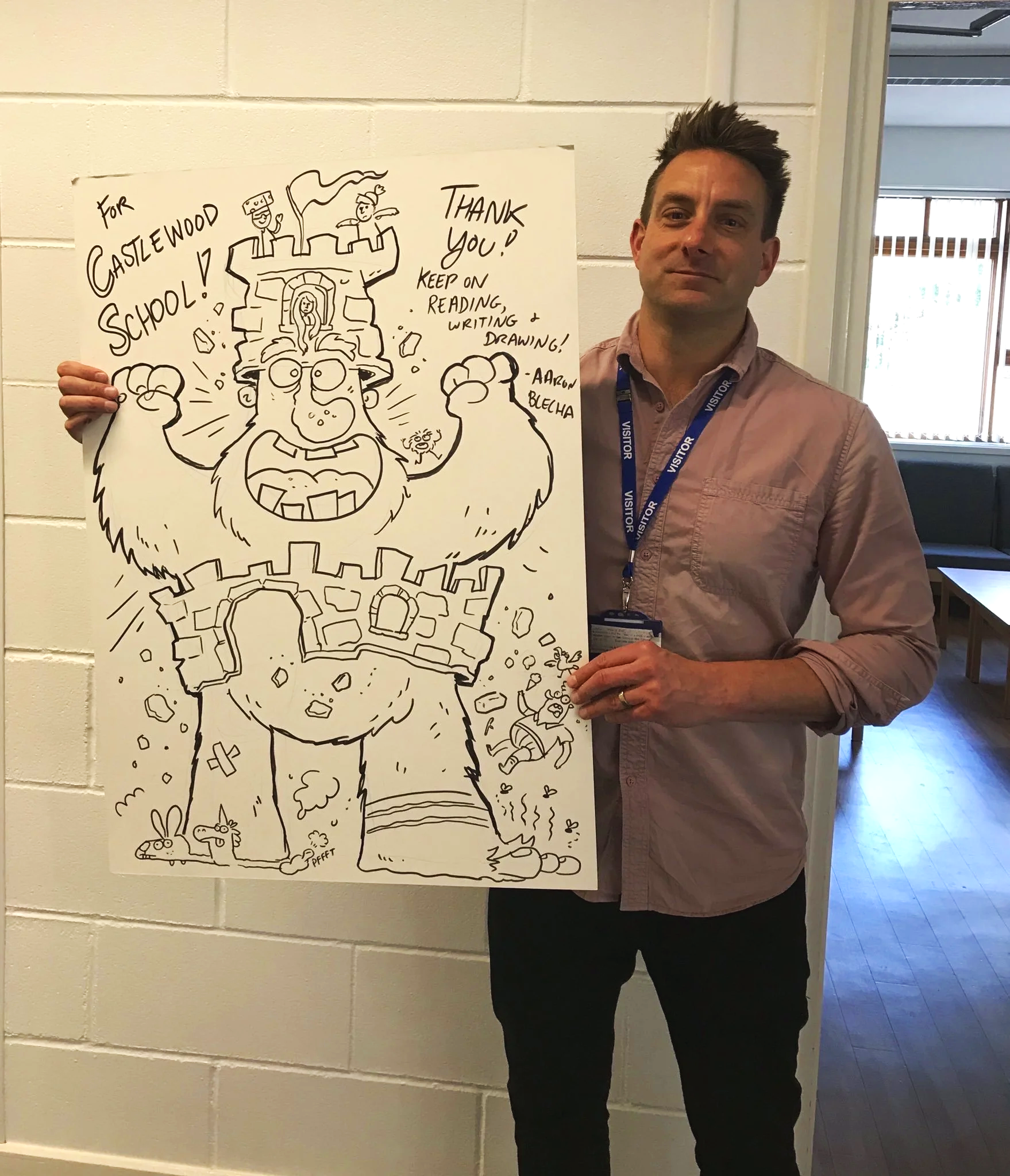 Photo of a man standing next to a large hand-drawn illustration on a whiteboard, depicting a cartoonish bearded giant with a castle on his head, holding a small girl and a tiny knight, with various smaller characters and animals at the bottom, and text expressing gratitude and encouragement to keep reading, writing, and drawing.