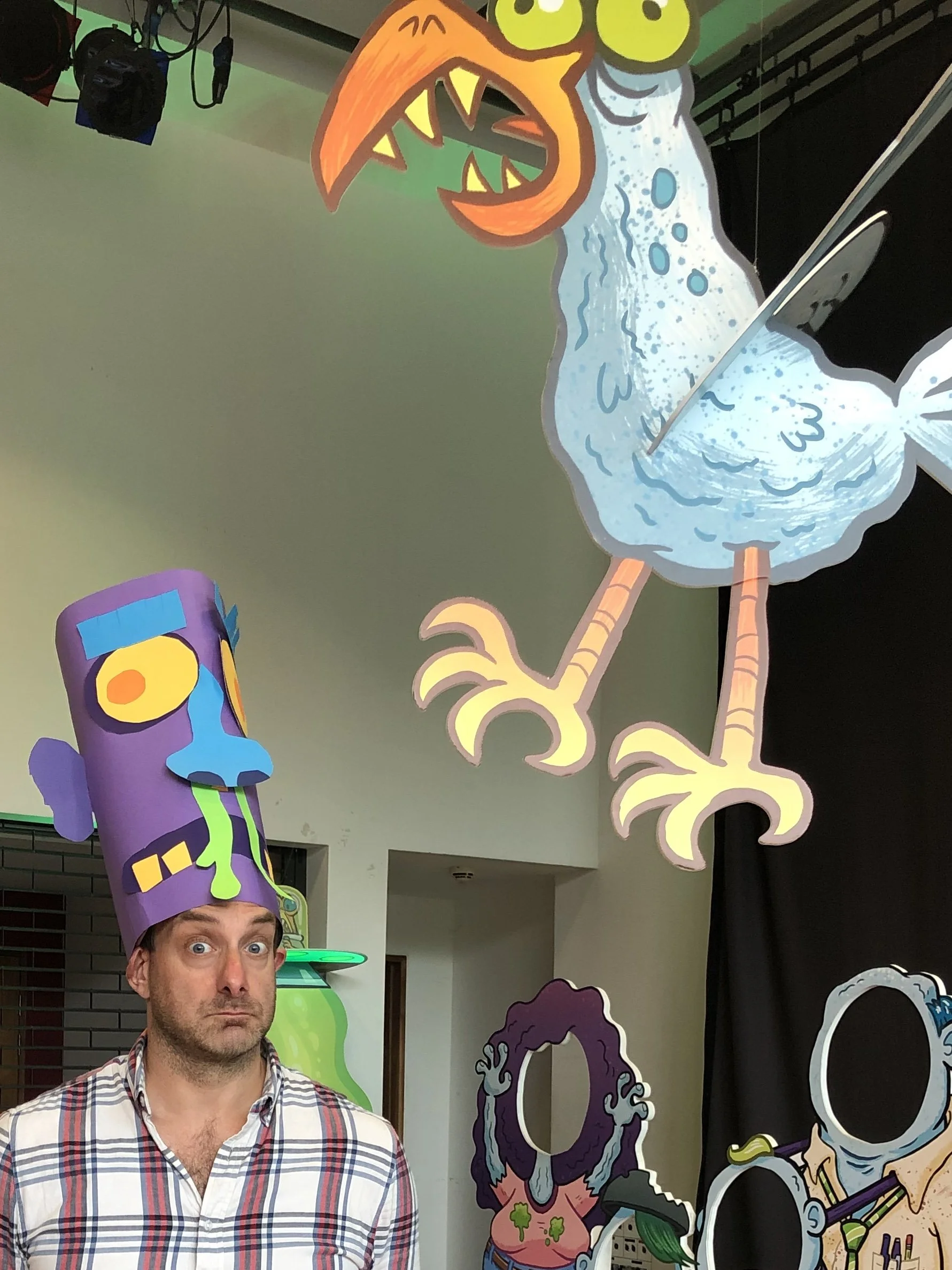 A man with surprised expression wearing a plaid shirt on a decorated background with cartoon characters and colorful props.