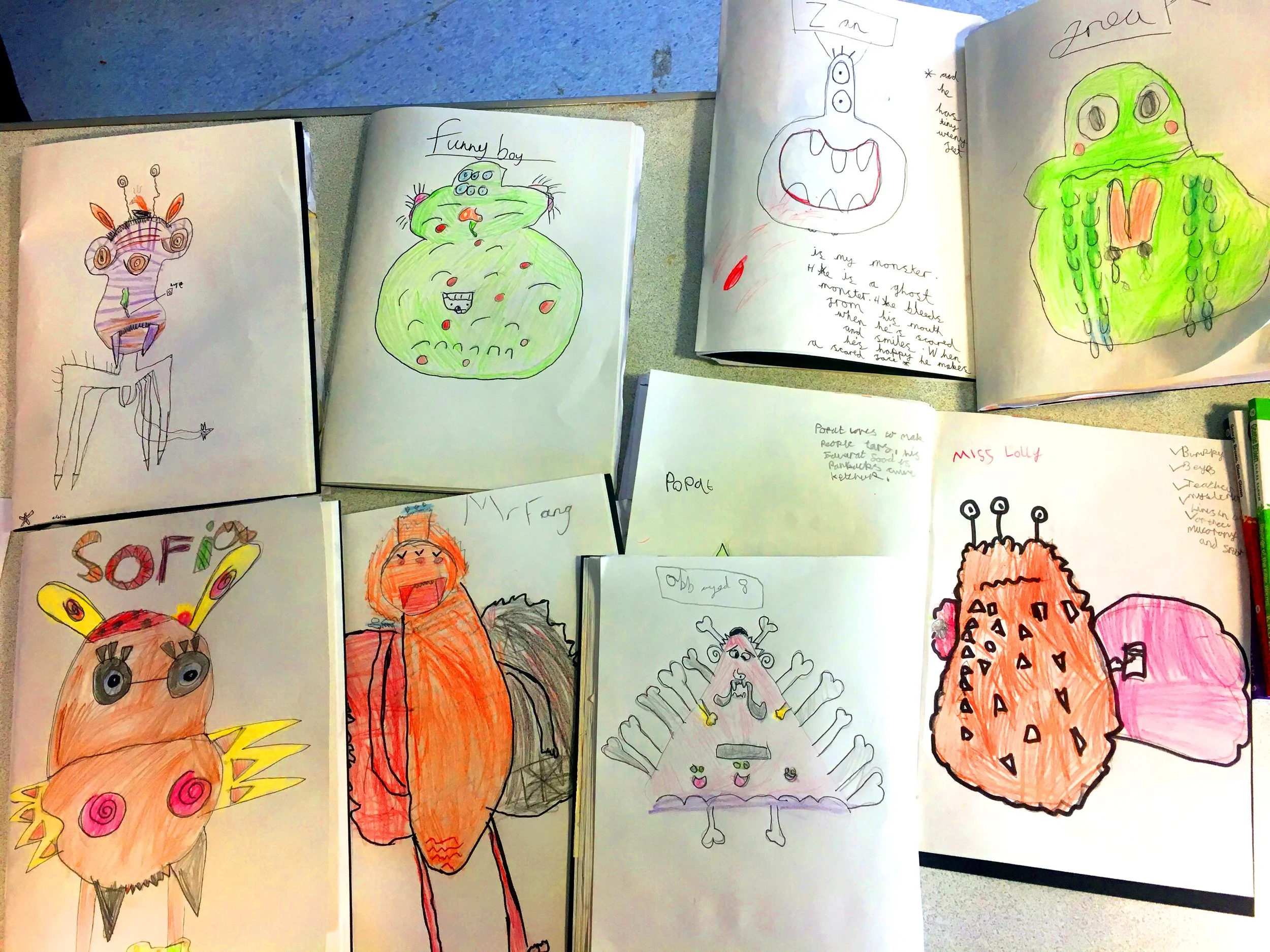 Collection of children's drawings of monsters and creatures with colorful markers and pencils.