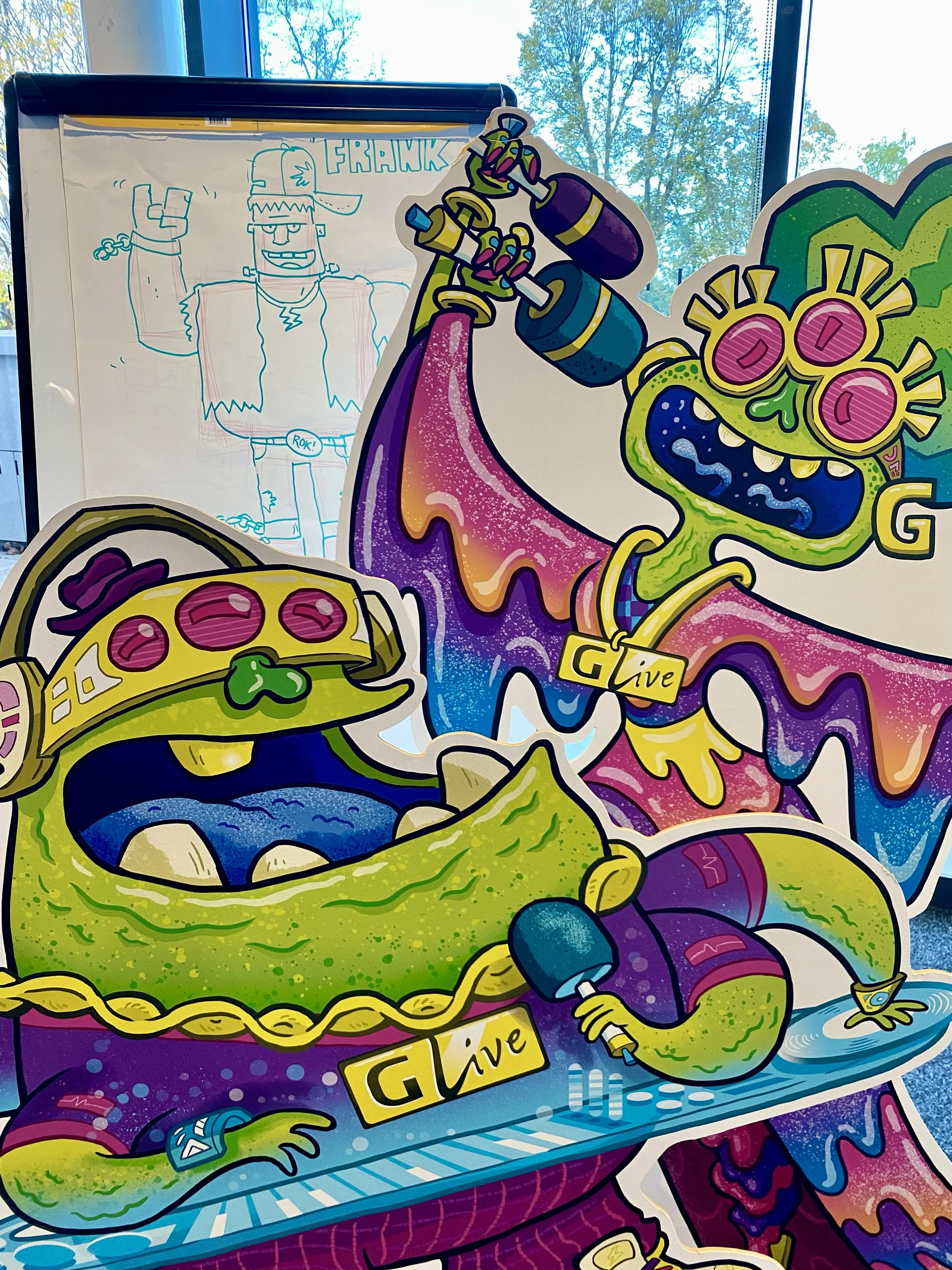 Colorful illustration of a cartoon alien with green skin and pink eyes sitting at a desk and using a computer mouse, with other science-fiction themed elements around. In the background, a whiteboard with a blue line drawing of a humanoid figure wearing a cap and chain, with a speech bubble saying "FRAWK."