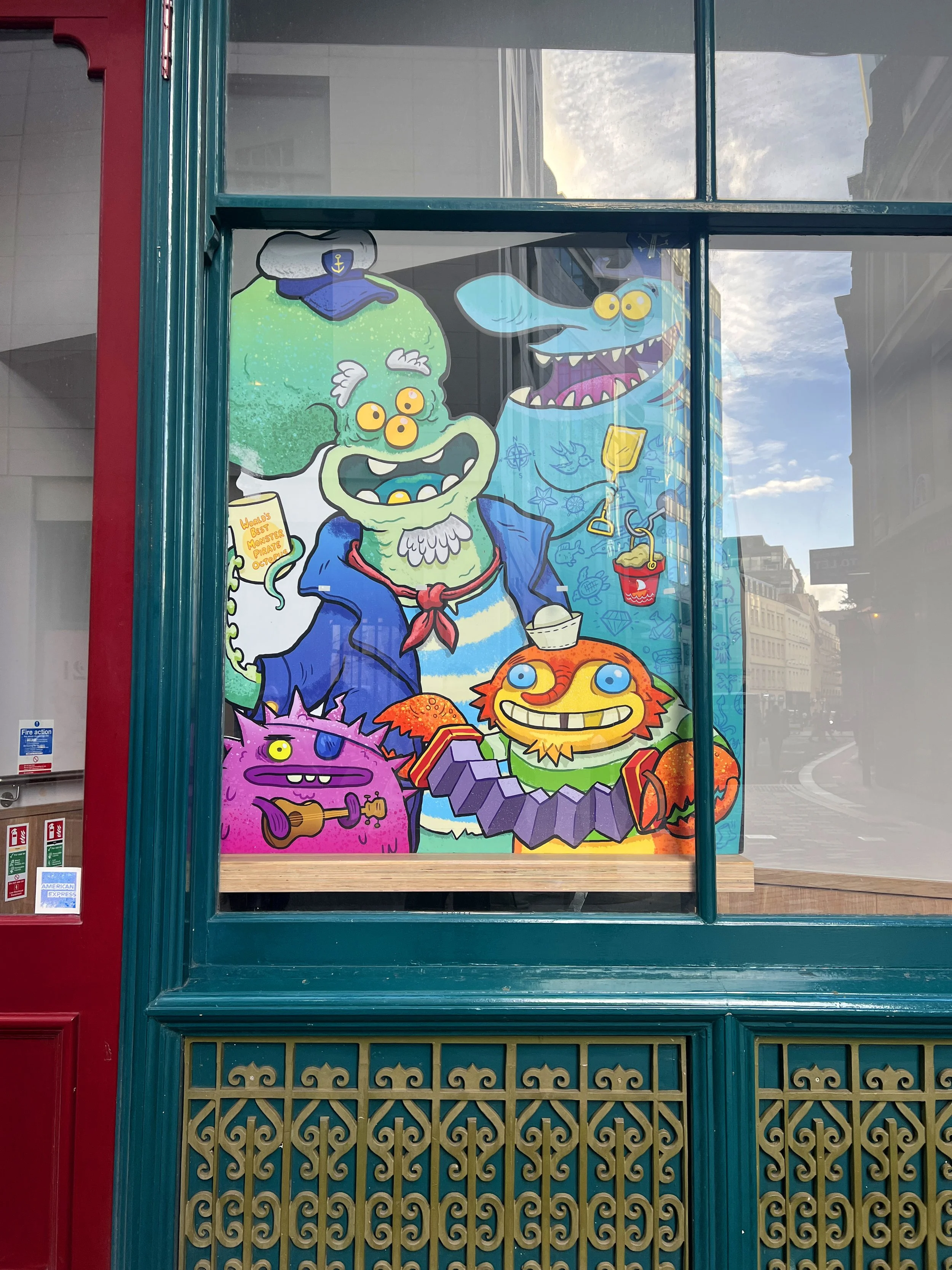 Colorful cartoon illustration of a sea monster holding a mug that says "World's Best Monster Pirate Octopus," with a blue whale with yellow eyes and sharp teeth, a pink monster with purple hair playing a guitar, and an orange fish with blue eyes and a mischievous grin, all set against a blue background with nautical symbols.