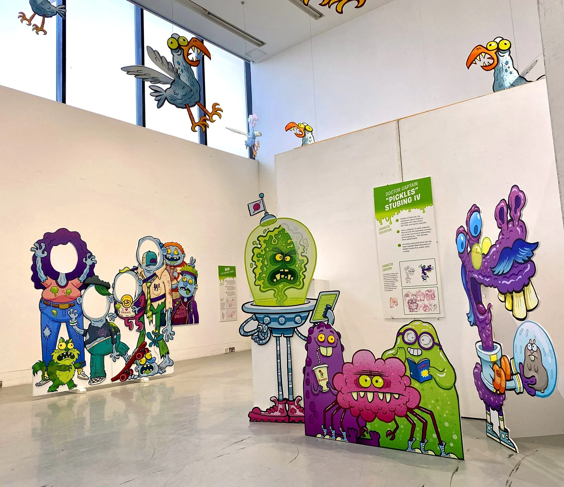 Colorful cartoon-style display of various monstrous characters with exaggerated features and vibrant colors at an art exhibit or gallery.