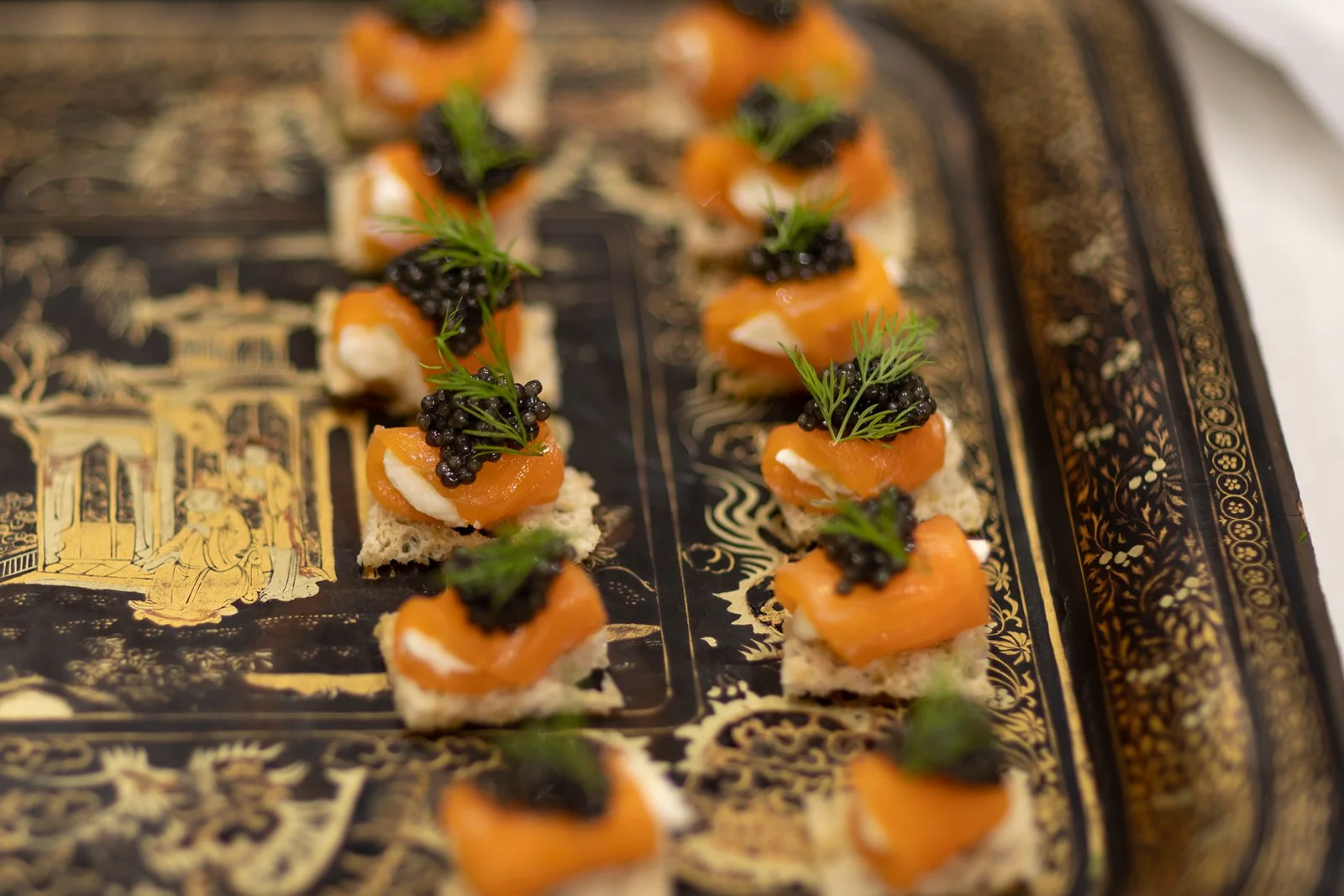 Canapes topped with smoked salmon, black caviar, and fresh herbs on a decorative gold and black tray.