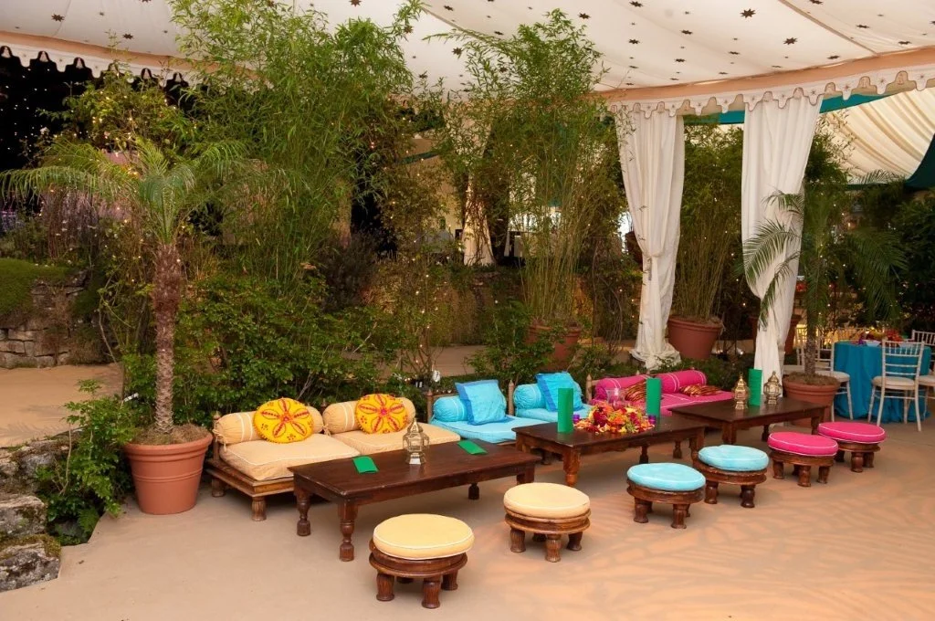 Outdoor party setup with colorful cushions, ottomans, and potted plants under a tent with star-patterned ceiling.