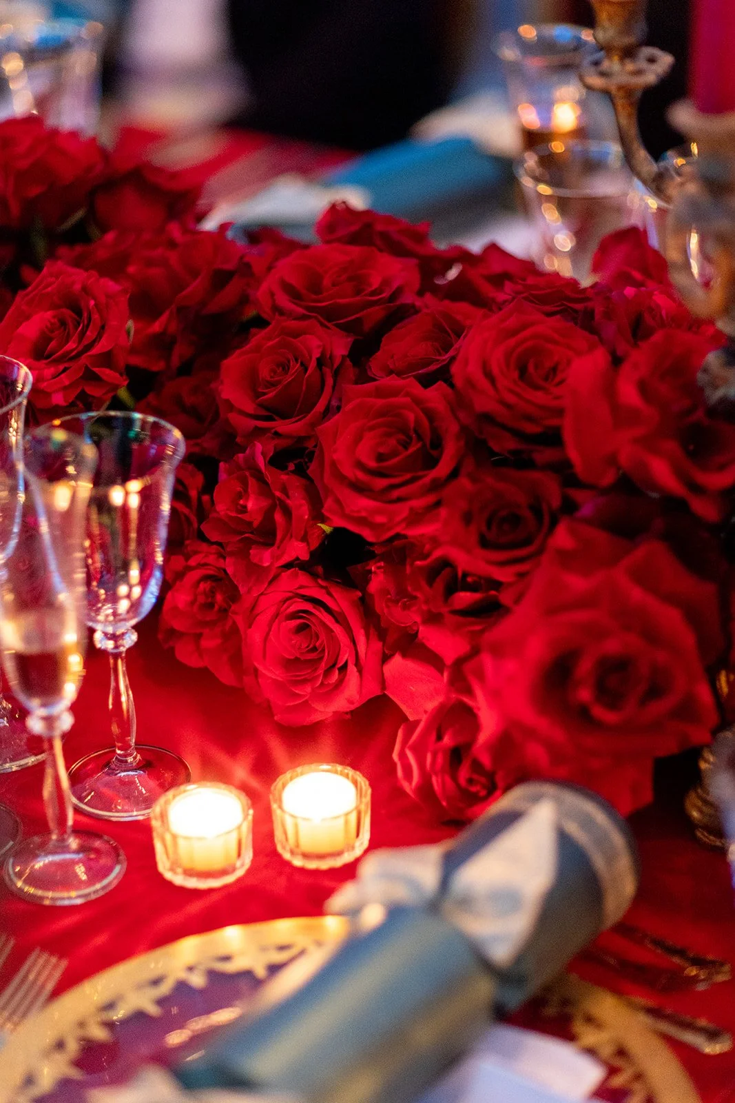 A table decorated with a large bouquet of red roses, candles, and glassware for a romantic or elegant setting.