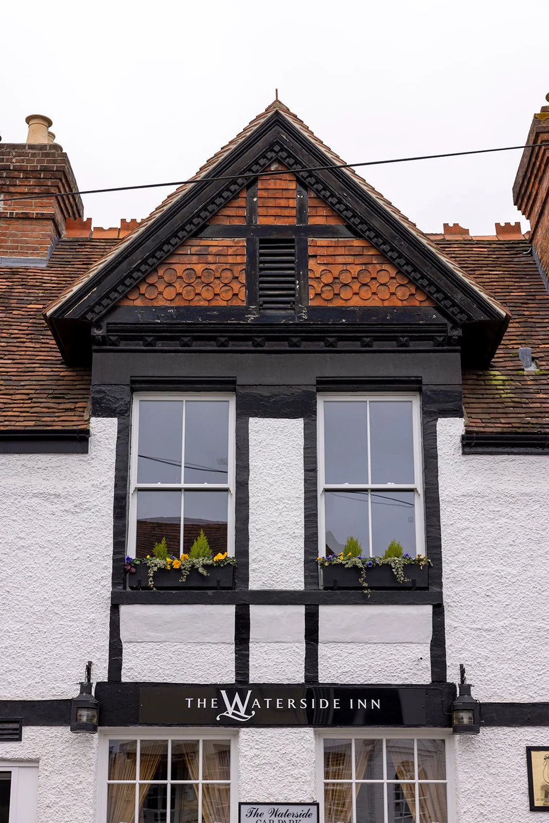 Front of The Waterside Inn, a building with black and white detail, two large windows with flower boxes, and a Tudor-style gable roof.