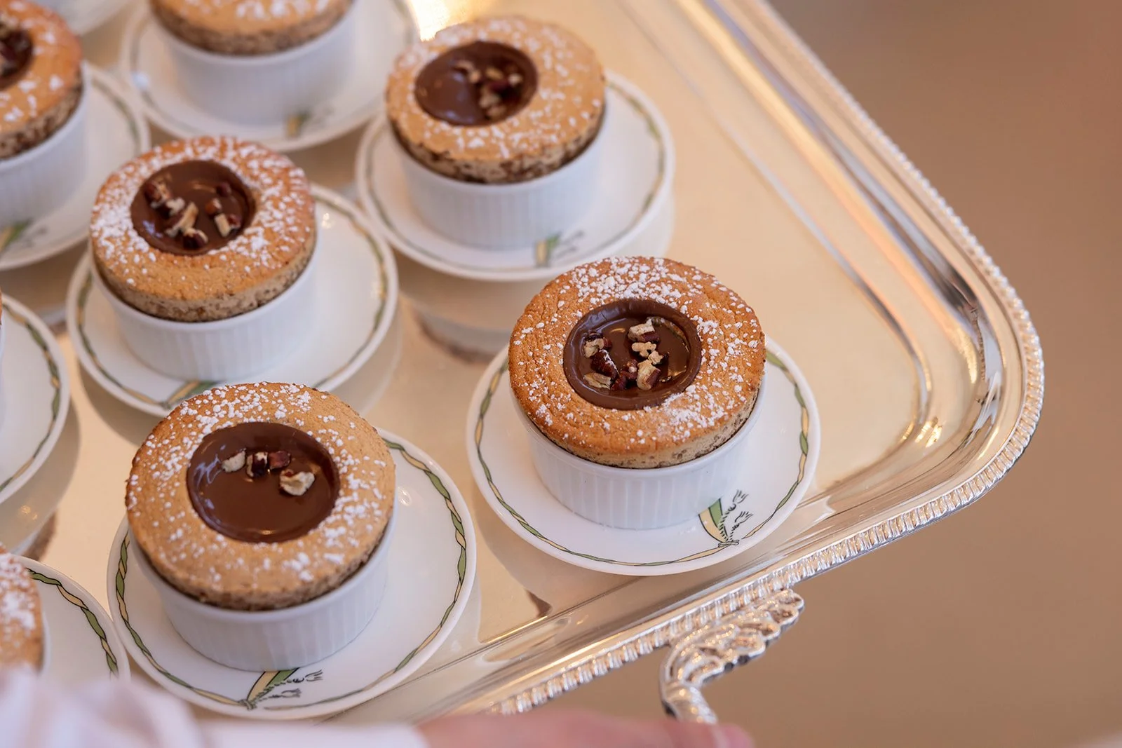 Several individual chocolate tarts with a cookie base, topped with a chocolate glaze and chopped nuts, served on white plates on a silver tray.