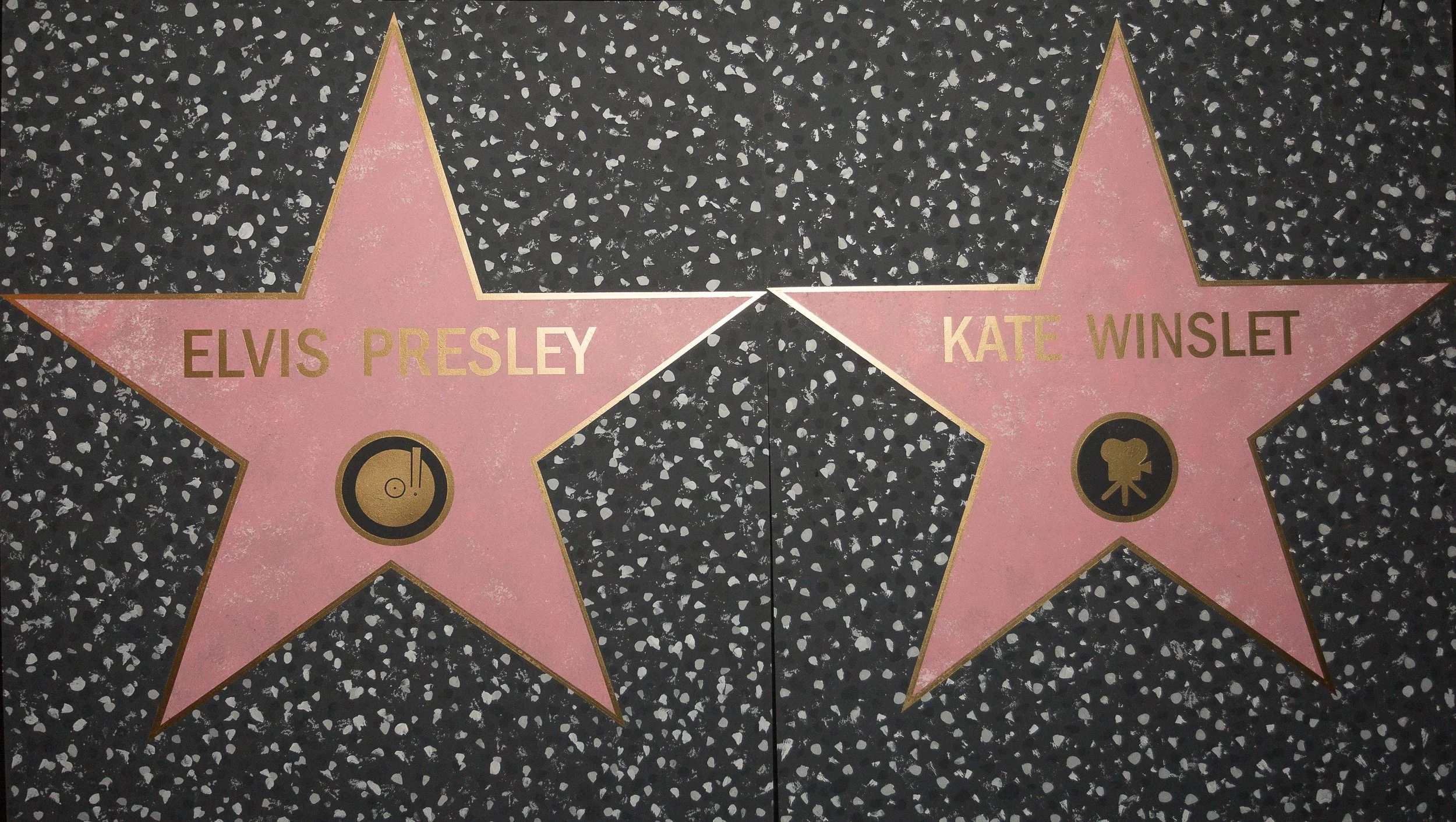 Two Hollywood Walk of Fame stars featuring Elvis Presley and Kate Winslet embedded in a black terrazzo sidewalk with white specks.