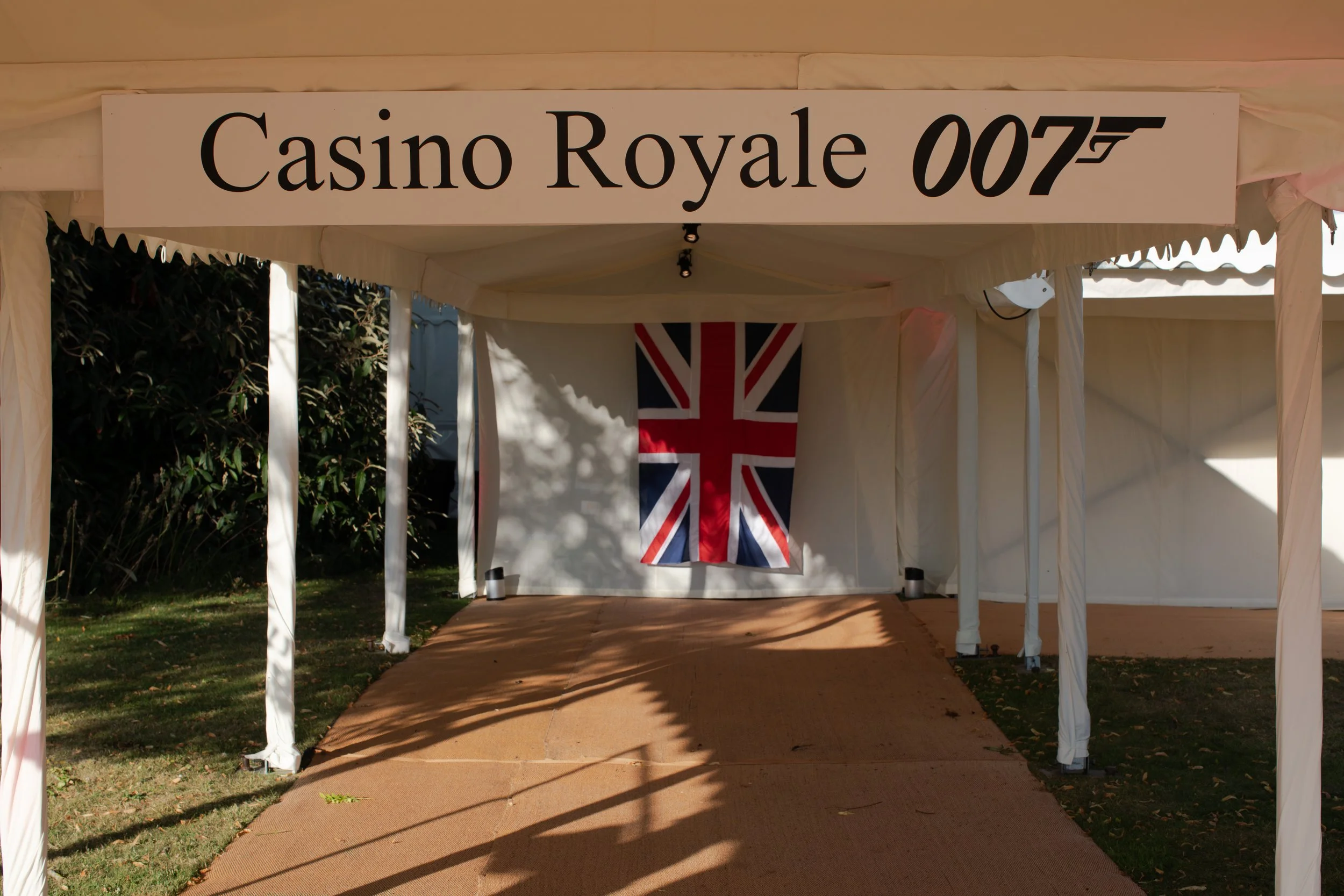 A white event tent with a sign reading 'Casino Royale 007' and a British flag hanging inside.