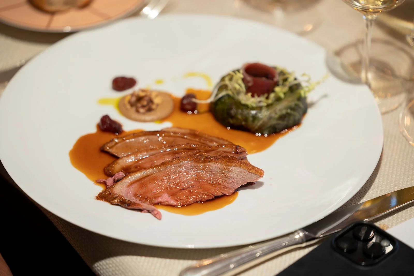 Plate with sliced duck breast, a small stuffed vegetable, and a garnish on a white plate at a dining table.