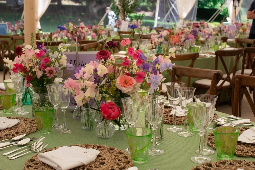A decorated banquet table with floral centerpieces, glassware, and plates at a party or wedding event.