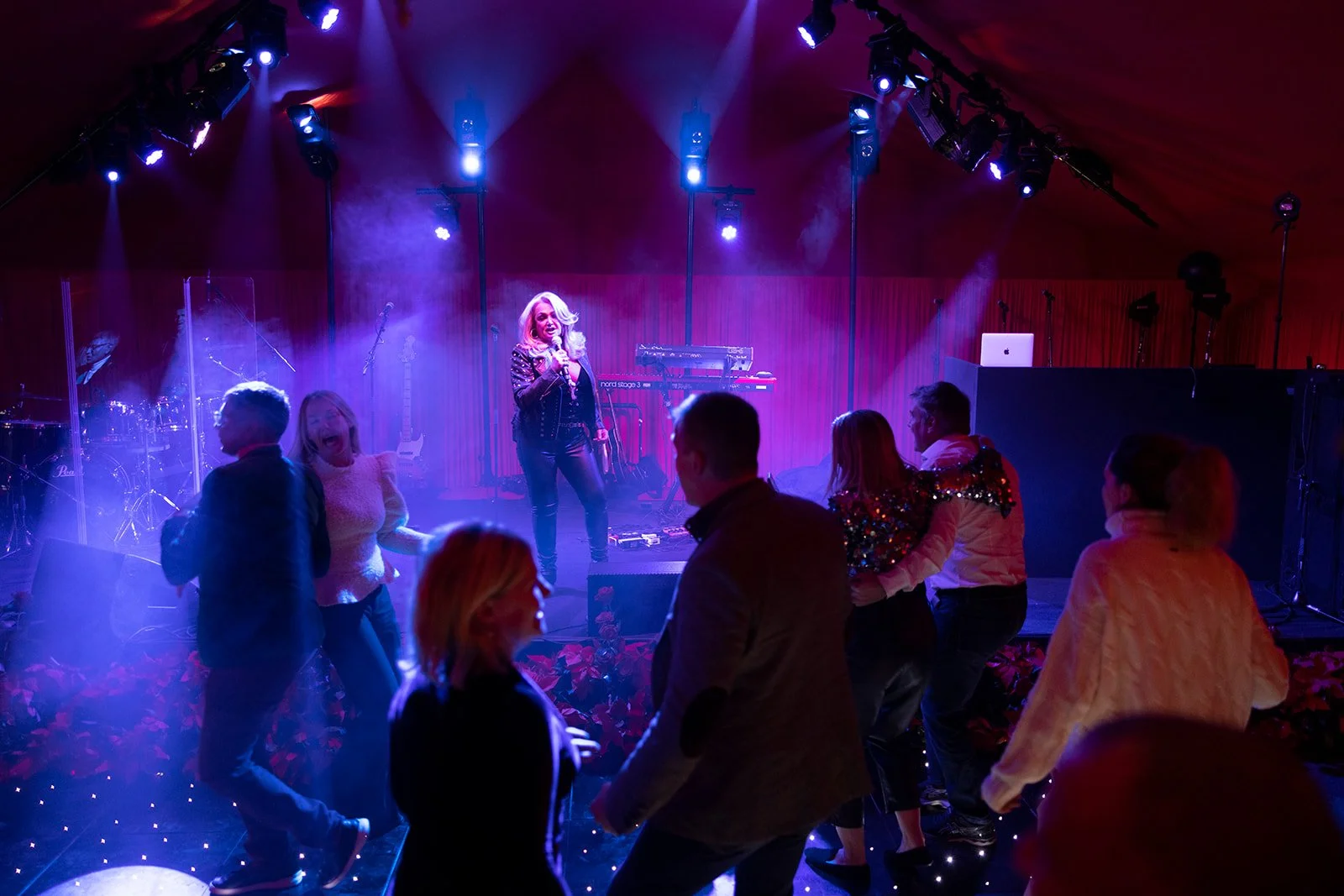 People dancing and a singer performing on stage in a nightclub or concert setting with purple and blue lighting.